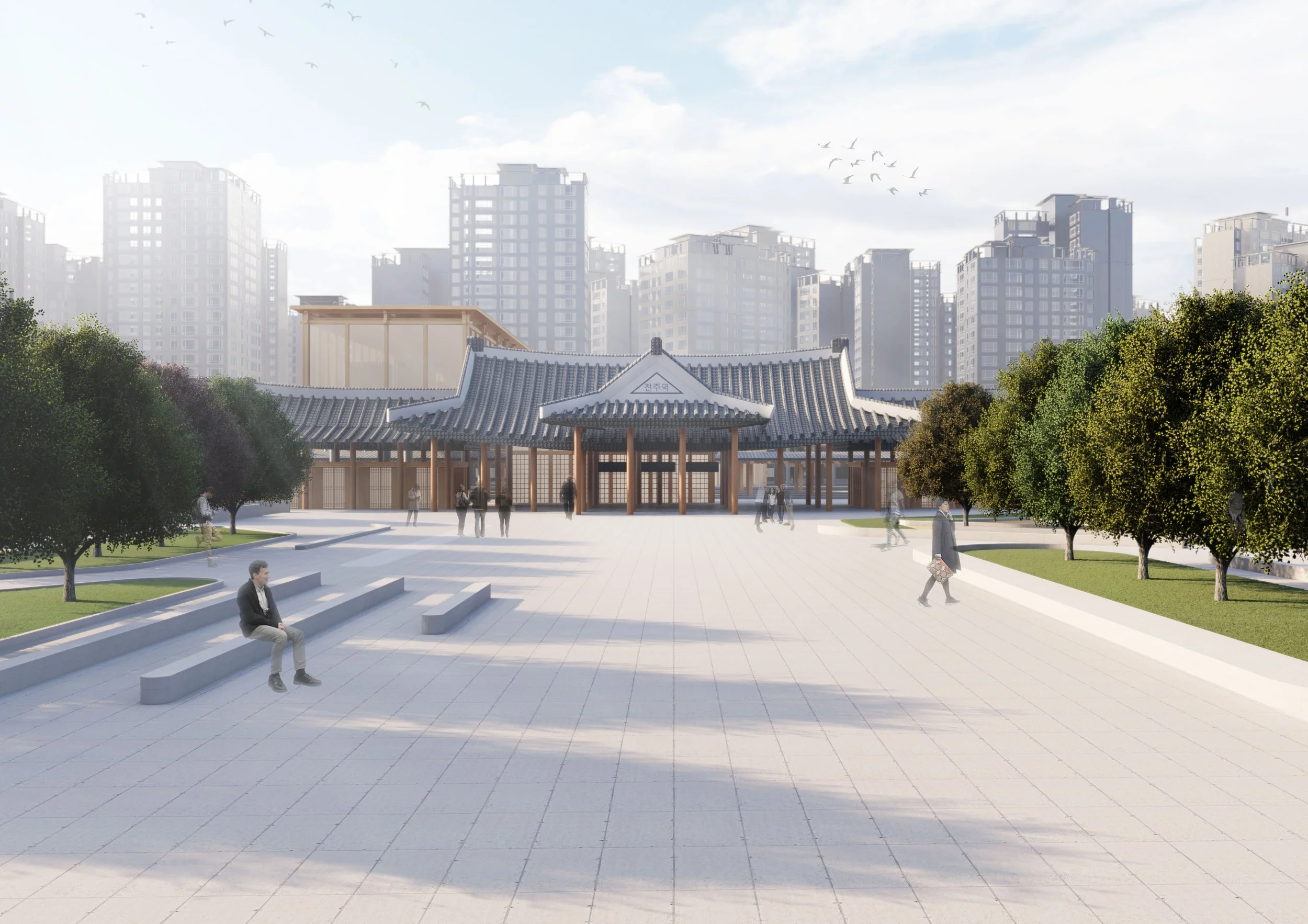 A traditional Korean-style pavilion with curved gray tiled roof and wooden pillars, surrounded by trees and an open paved plaza in an urban park, with high-rise buildings in the background and people walking and sitting.