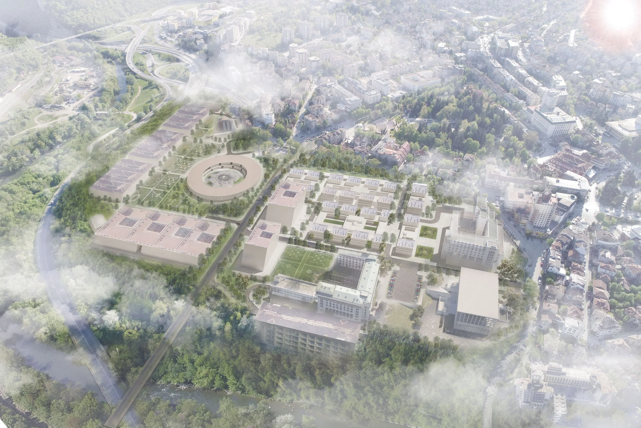 Aerial view of an urban area with a large campus featuring multiple modern buildings, green spaces, walking paths, and a circular structure surrounded by trees, with a highway and city streets in the background, partially obscured by clouds and fog.