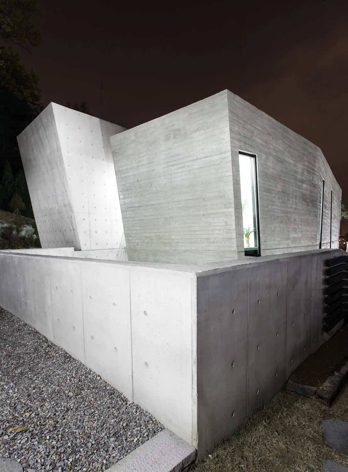 Modern concrete building with angled design and narrow windows, nighttime setting.
