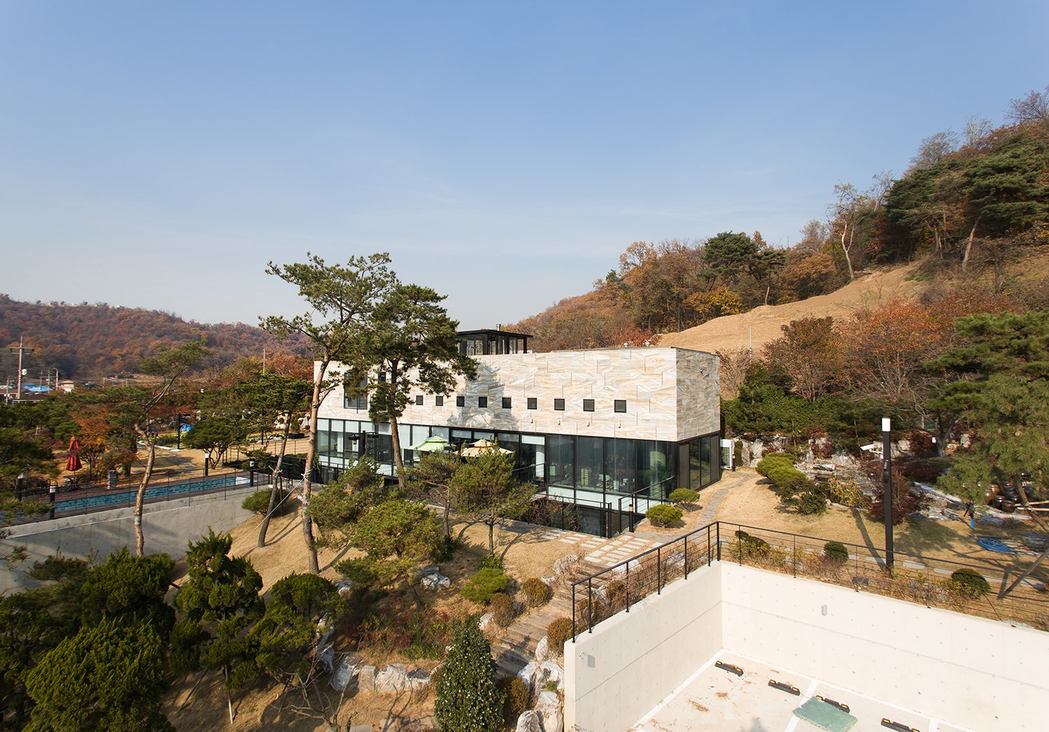 Modern building with glass windows and a stone facade surrounded by trees and hills in the background.