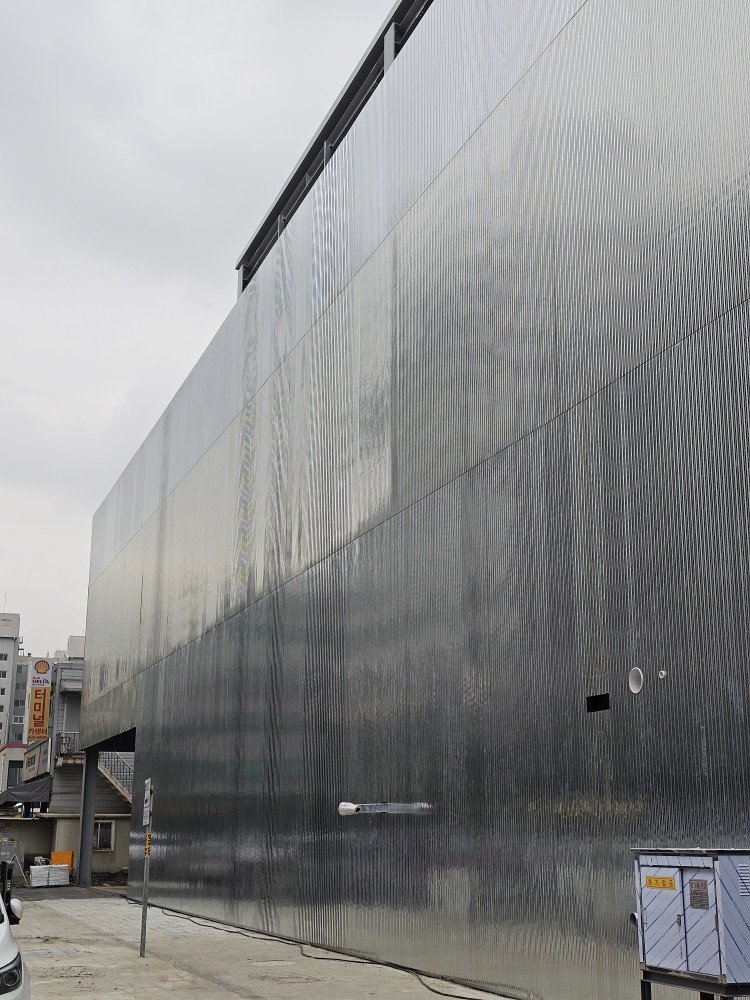 A large modern building with a shiny, reflective metal exterior, with a parking lot and cityscape in the background.