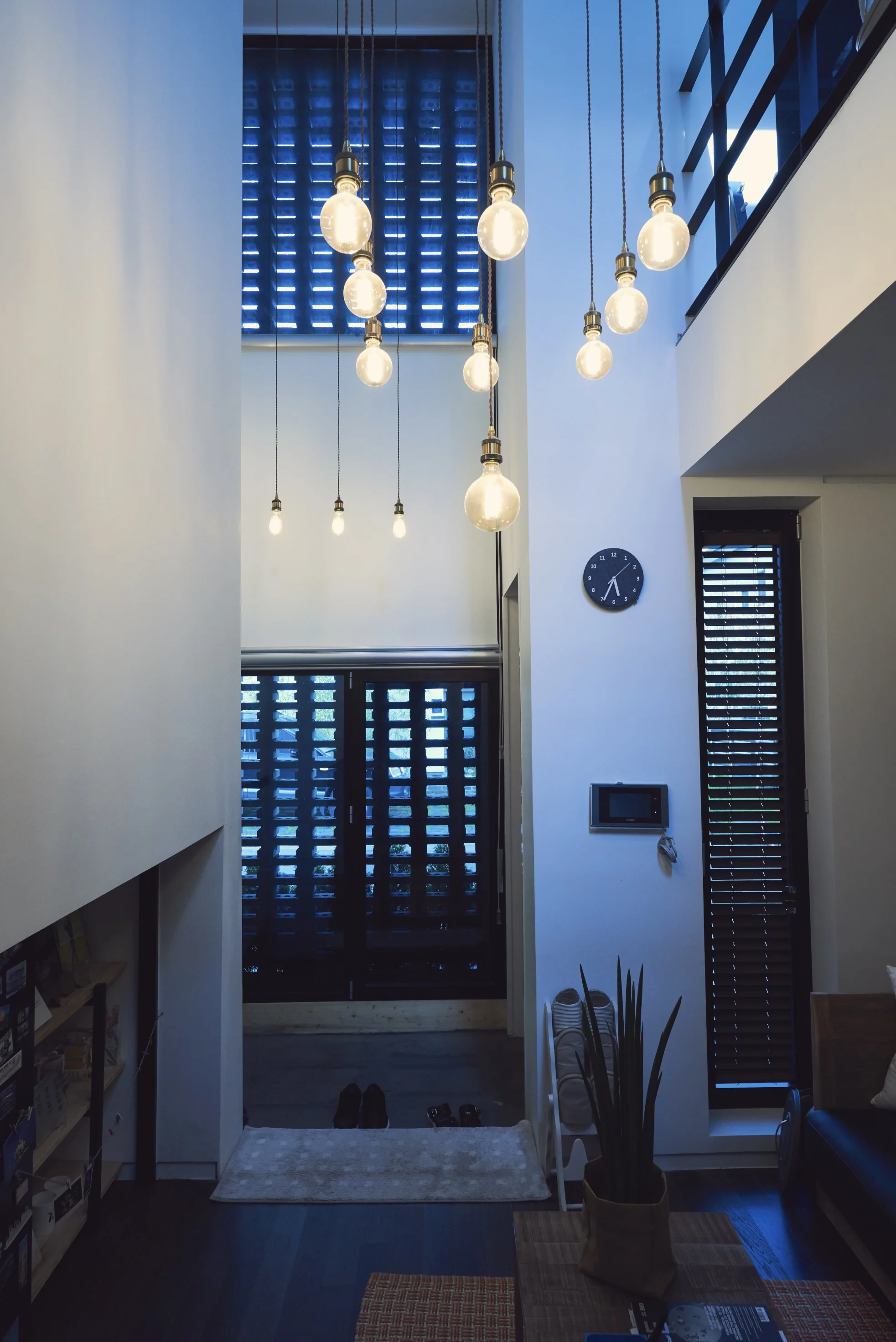 Interior view of modern home entrance with hanging light bulbs, blue window blinds, and a small clock on the wall.