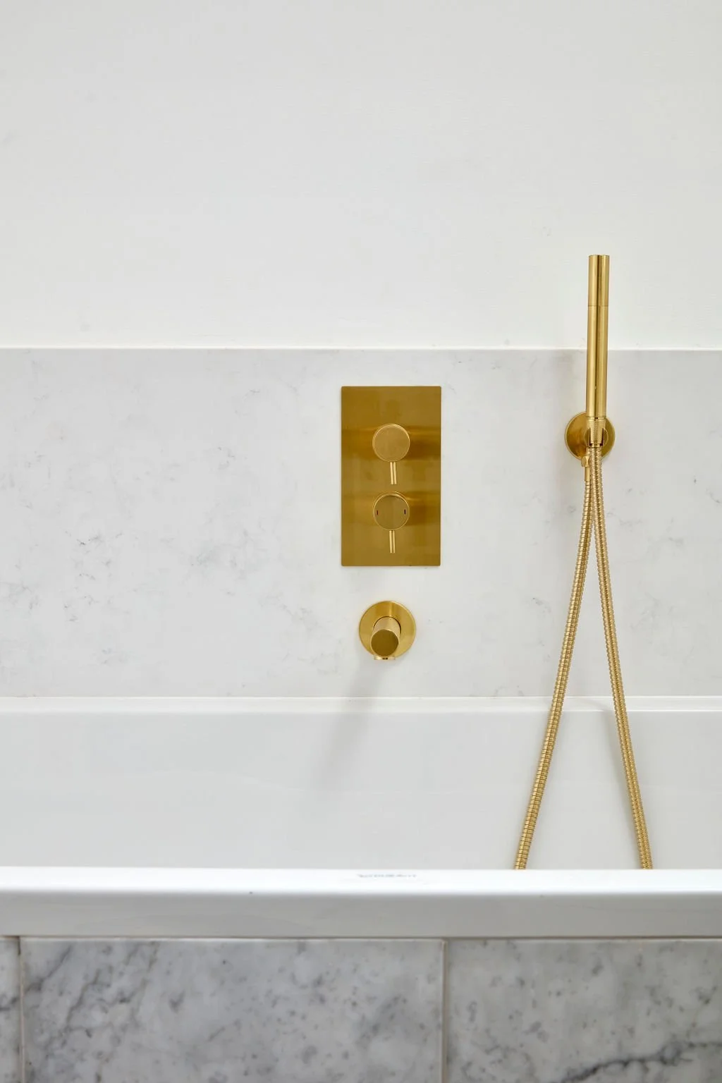 Gold shower fixtures on a marble wall in a bathroom.
