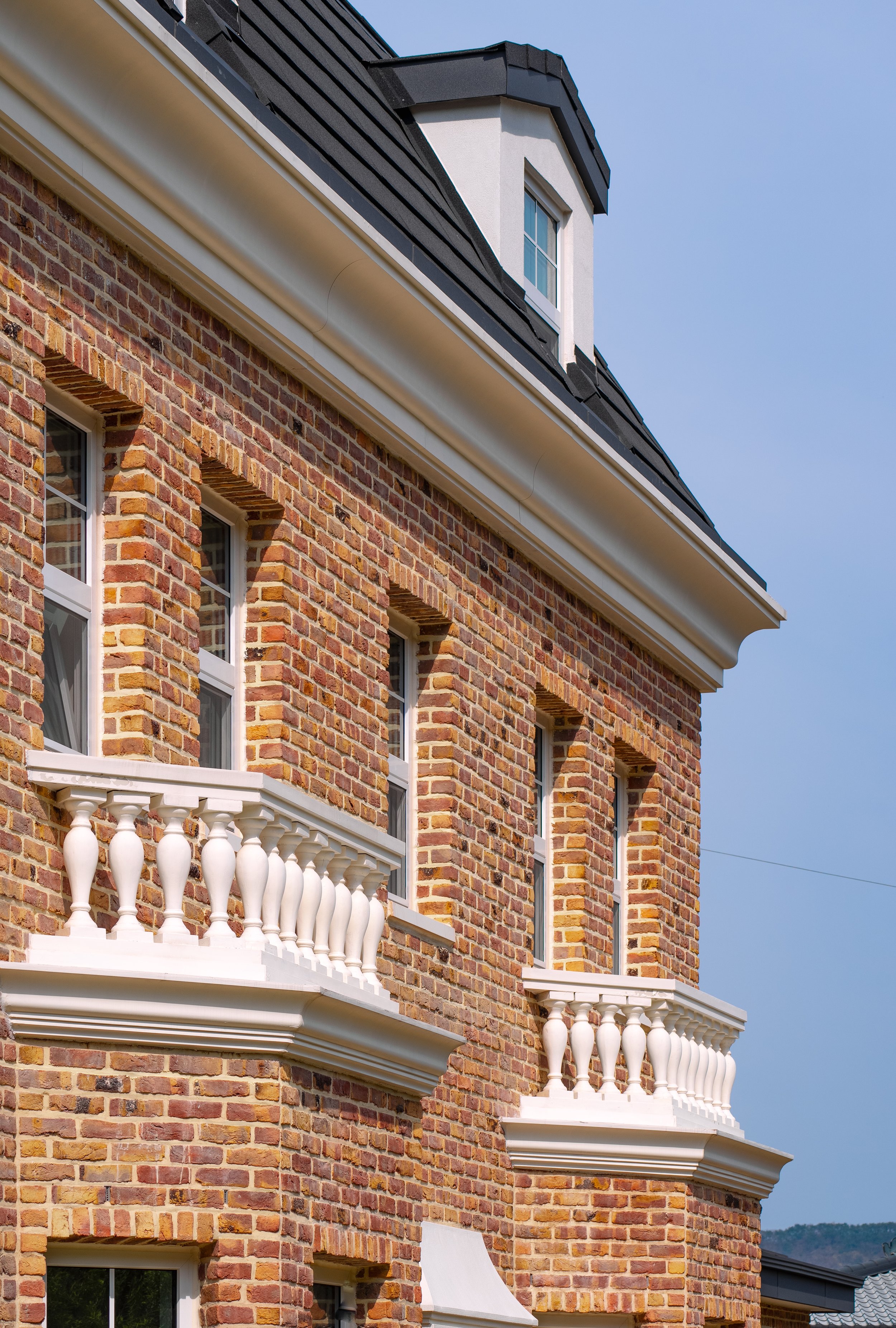 Close-up of a brick building with white decorative balconies and a dormer window on the roof.