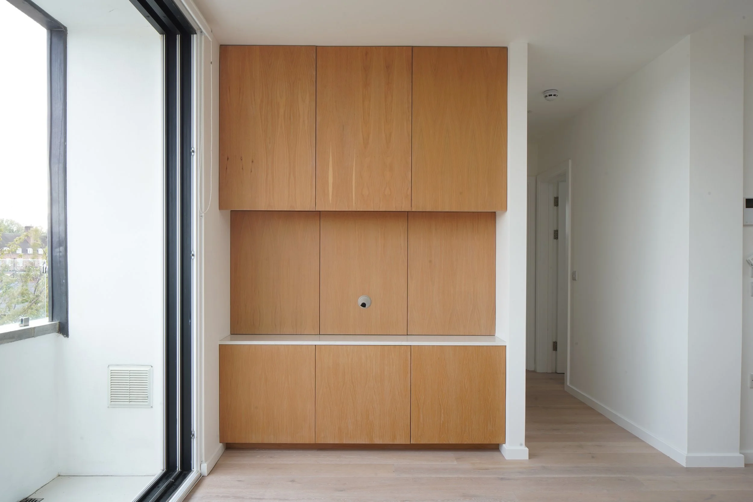Modern built-in wooden cabinets on white wall in minimalistic room next to glass door leading outside