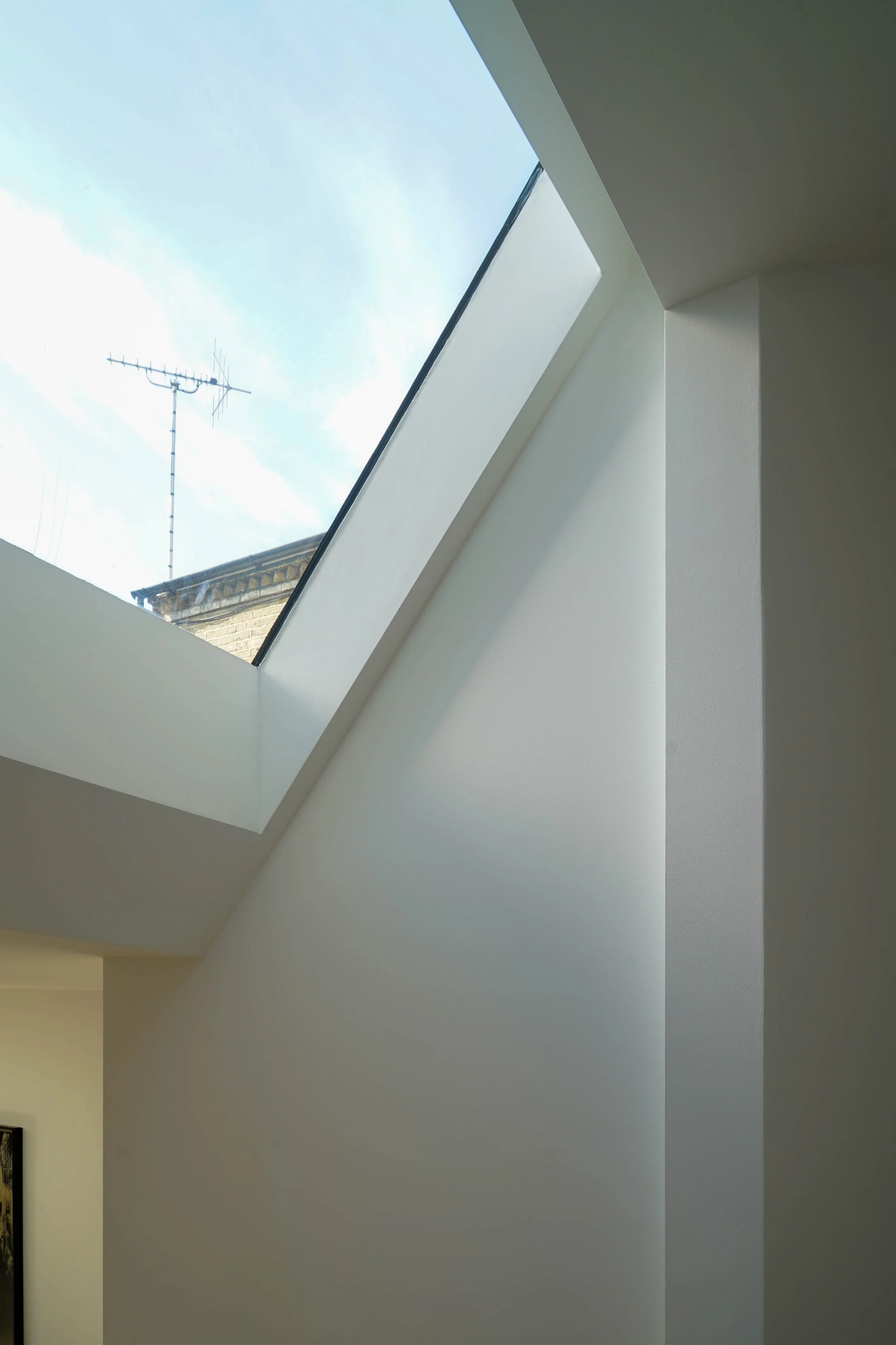 Interior view of a room with a skylight window on a sloped ceiling, showing a blue sky and an antenna outside.