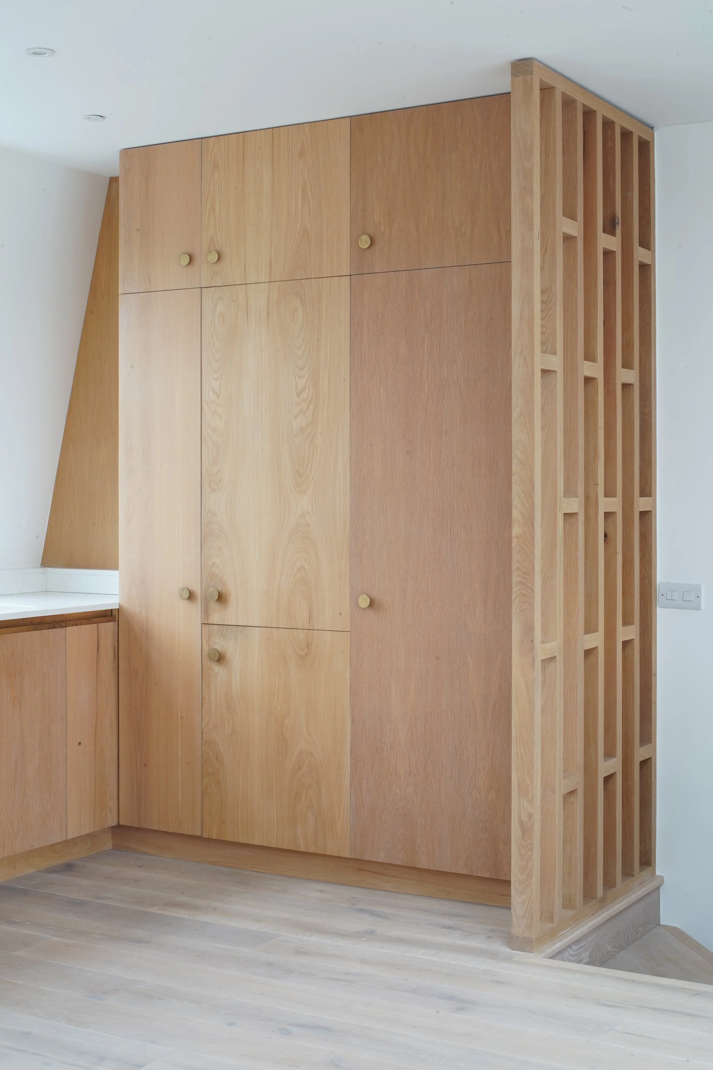 Wooden built-in cabinetry with cabinet doors and open grid shelving on the side, in a modern interior.