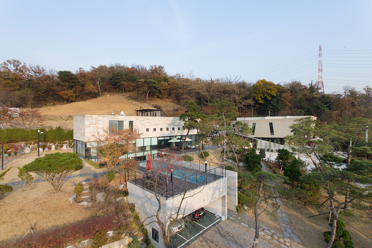 Aerial view of modern apartment complex with a swimming pool, surrounded by trees and hills.
