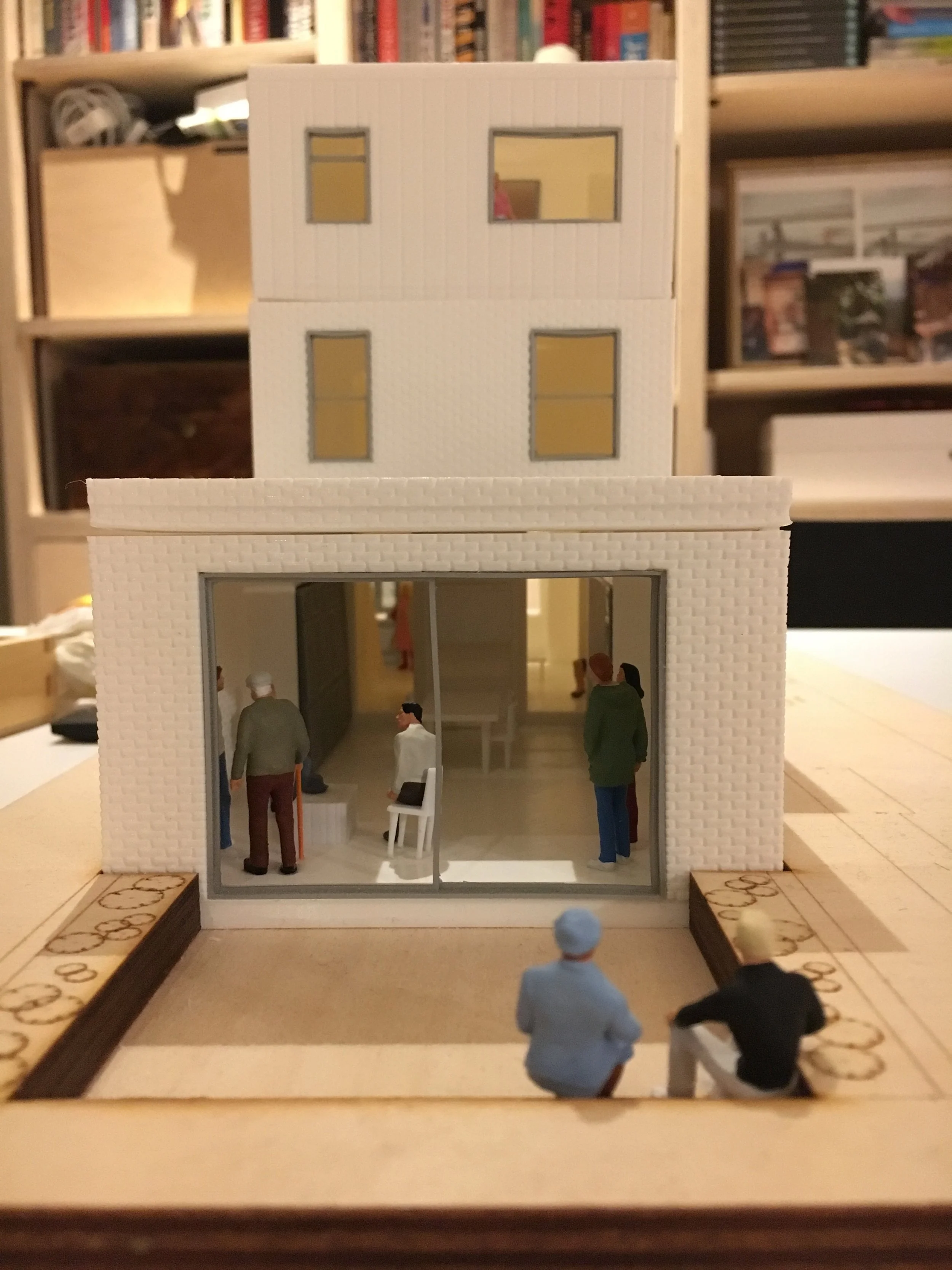 Miniature architectural model of a modern multi-story building with detailed interior figures and surrounding landscape elements.
