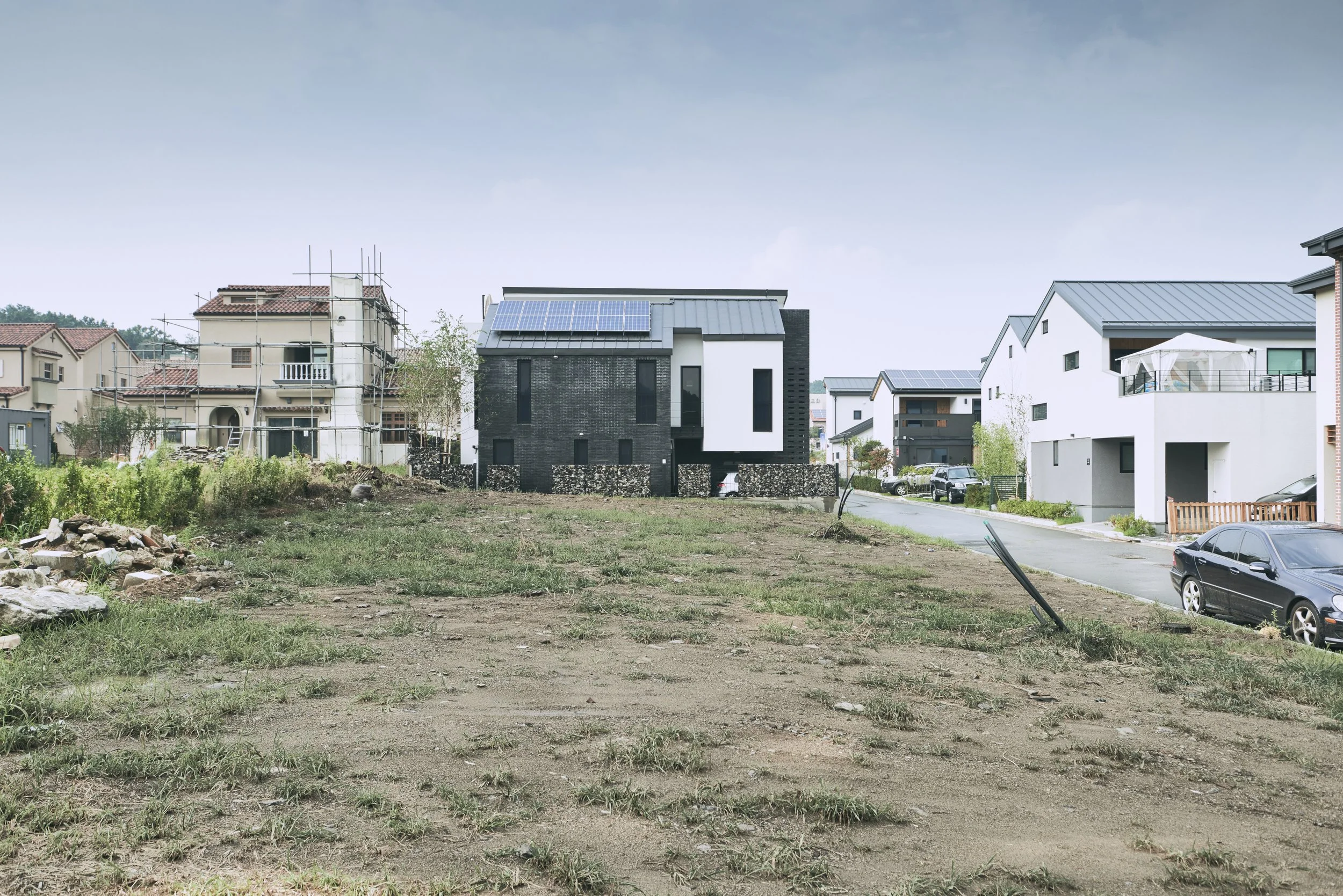 A residential neighborhood with modern houses, some under construction, and an open patch of land in the foreground.