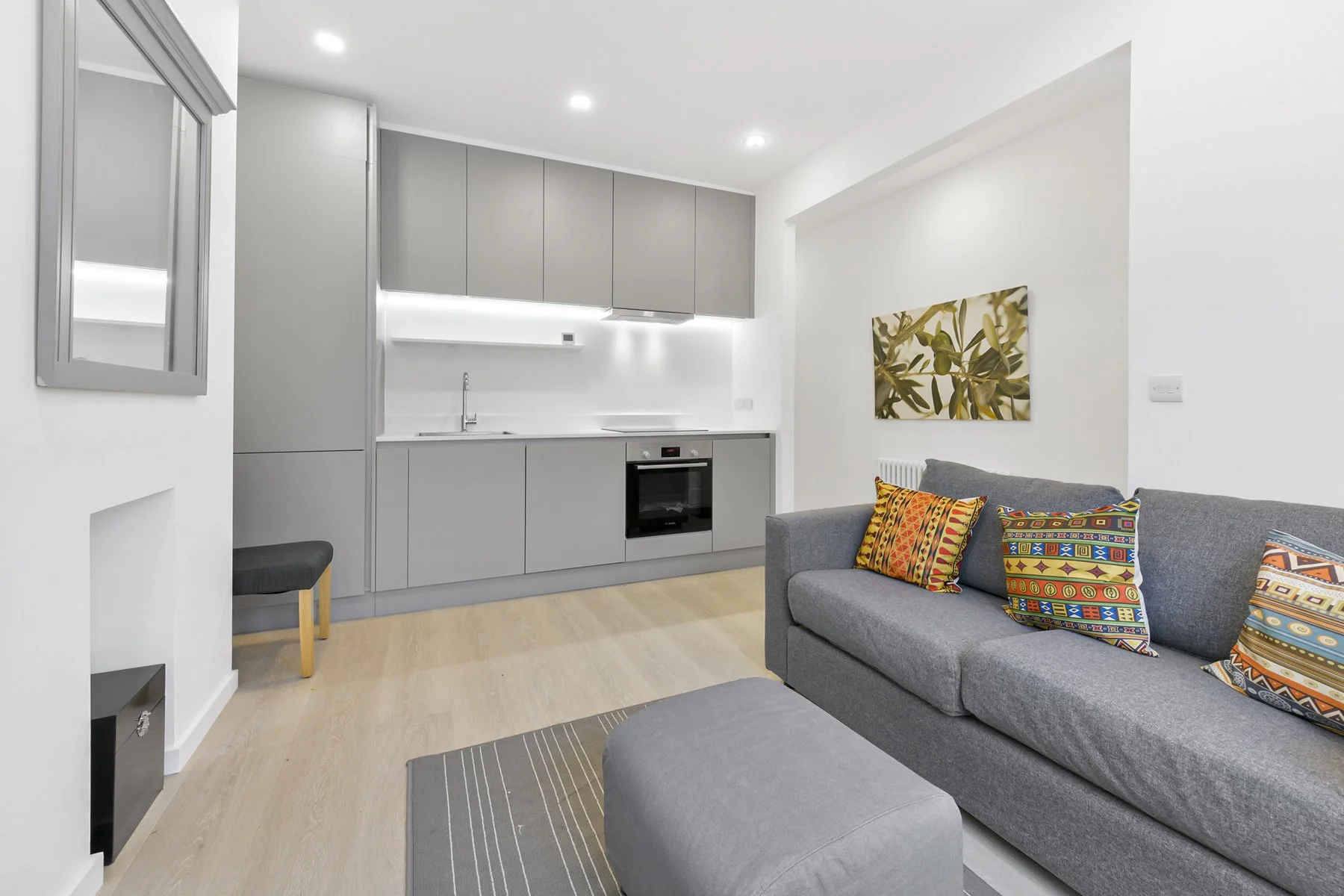 Modern living room and kitchen with gray cabinetry, colorful pillows on a gray sofa, and minimalist decor.