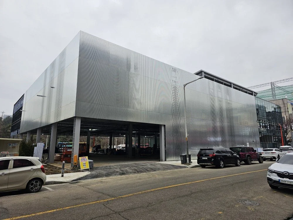 Modern multi-story building with a metallic exterior and parking area in front.