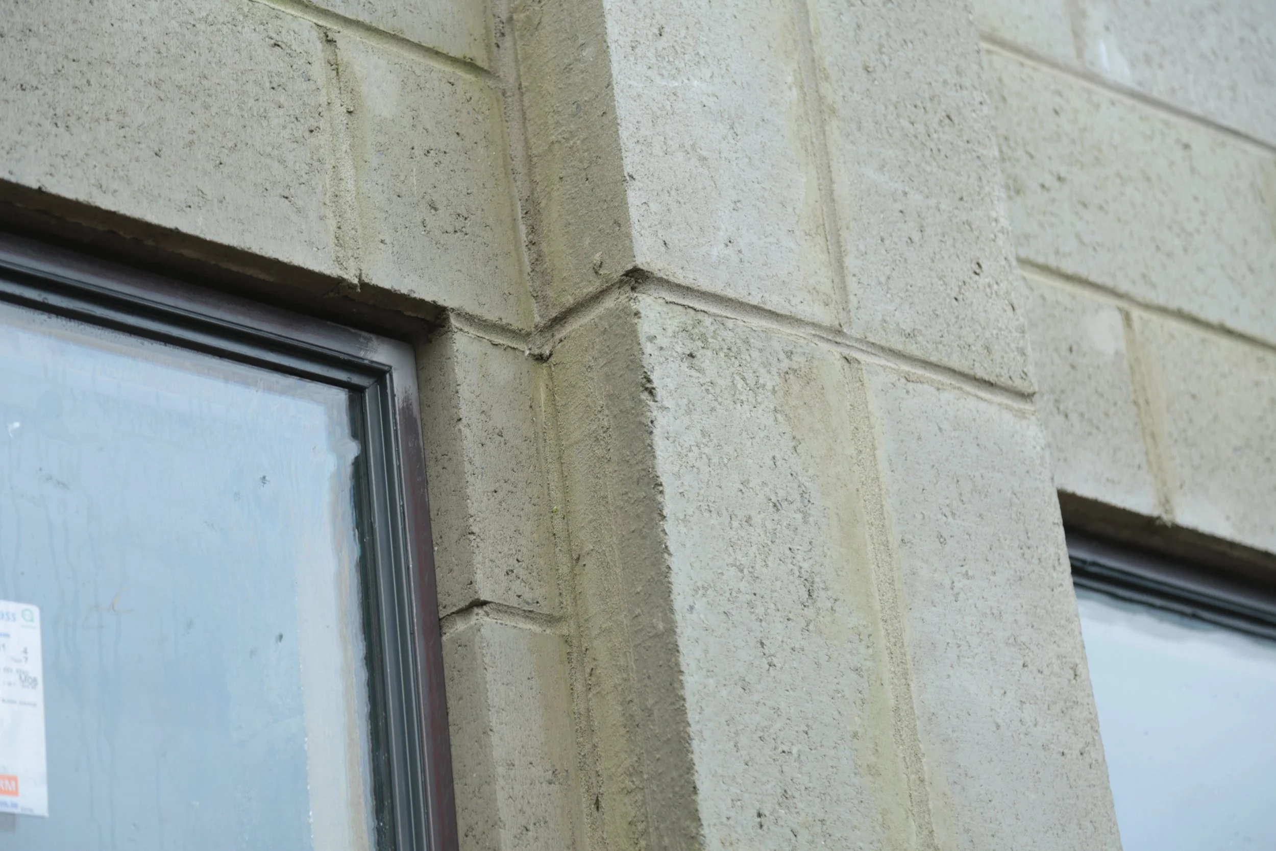 Close-up of the corner of a building with beige brick exterior and windows with dark trim.