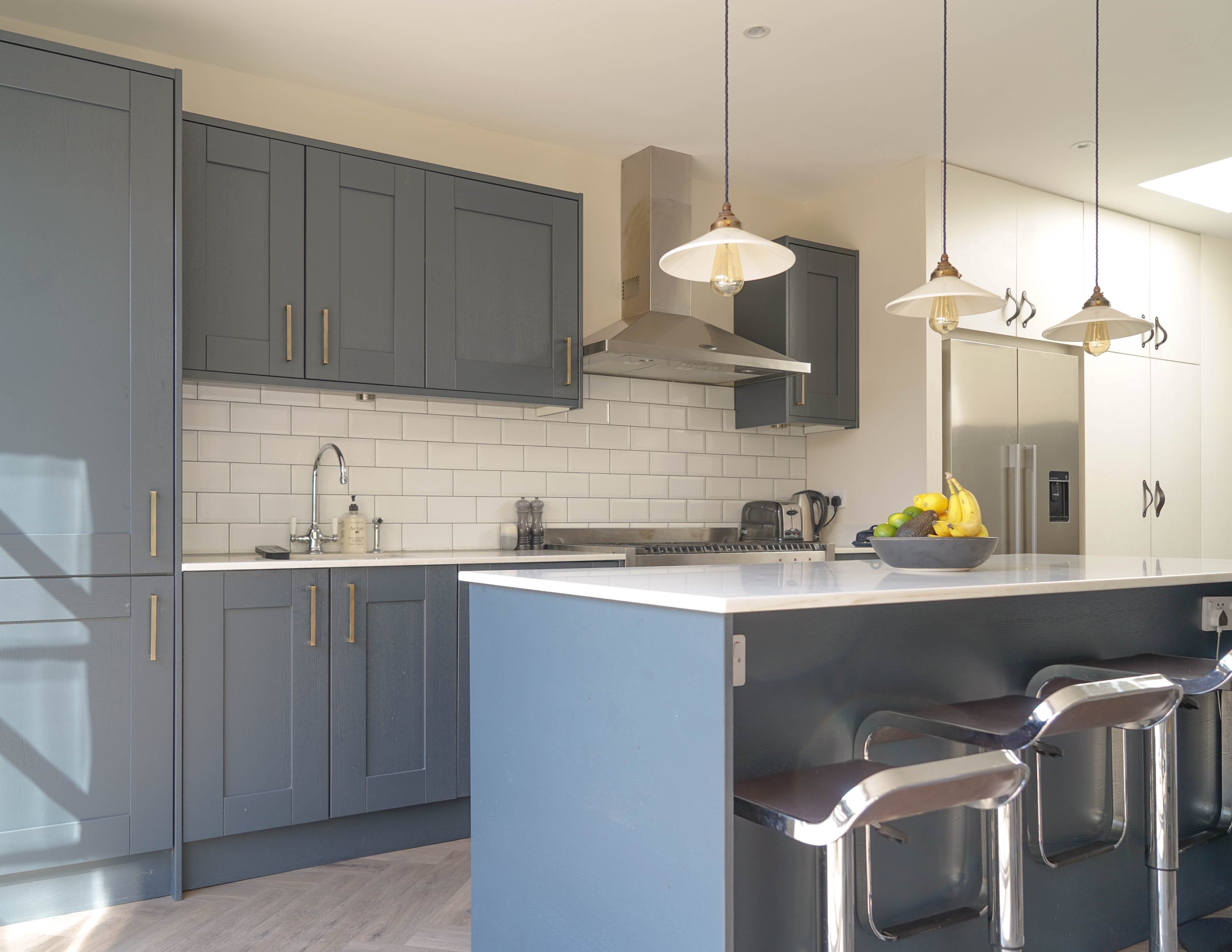 Modern kitchen with blue and white cabinets, white subway tile backsplash, stainless steel appliances, and a white countertop island with barstools.