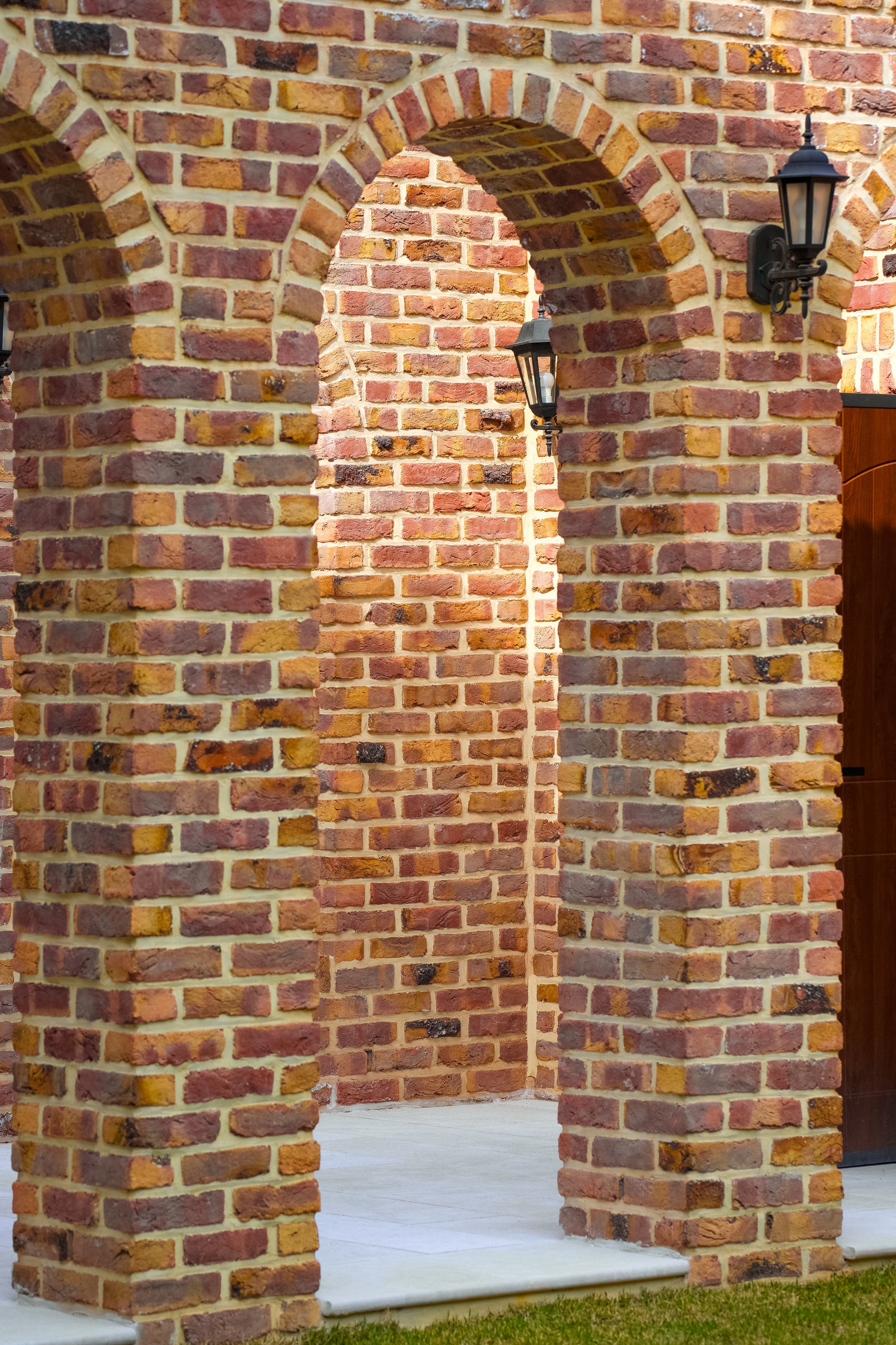 Brick archways with outdoor lanterns attached, part of a building exterior.