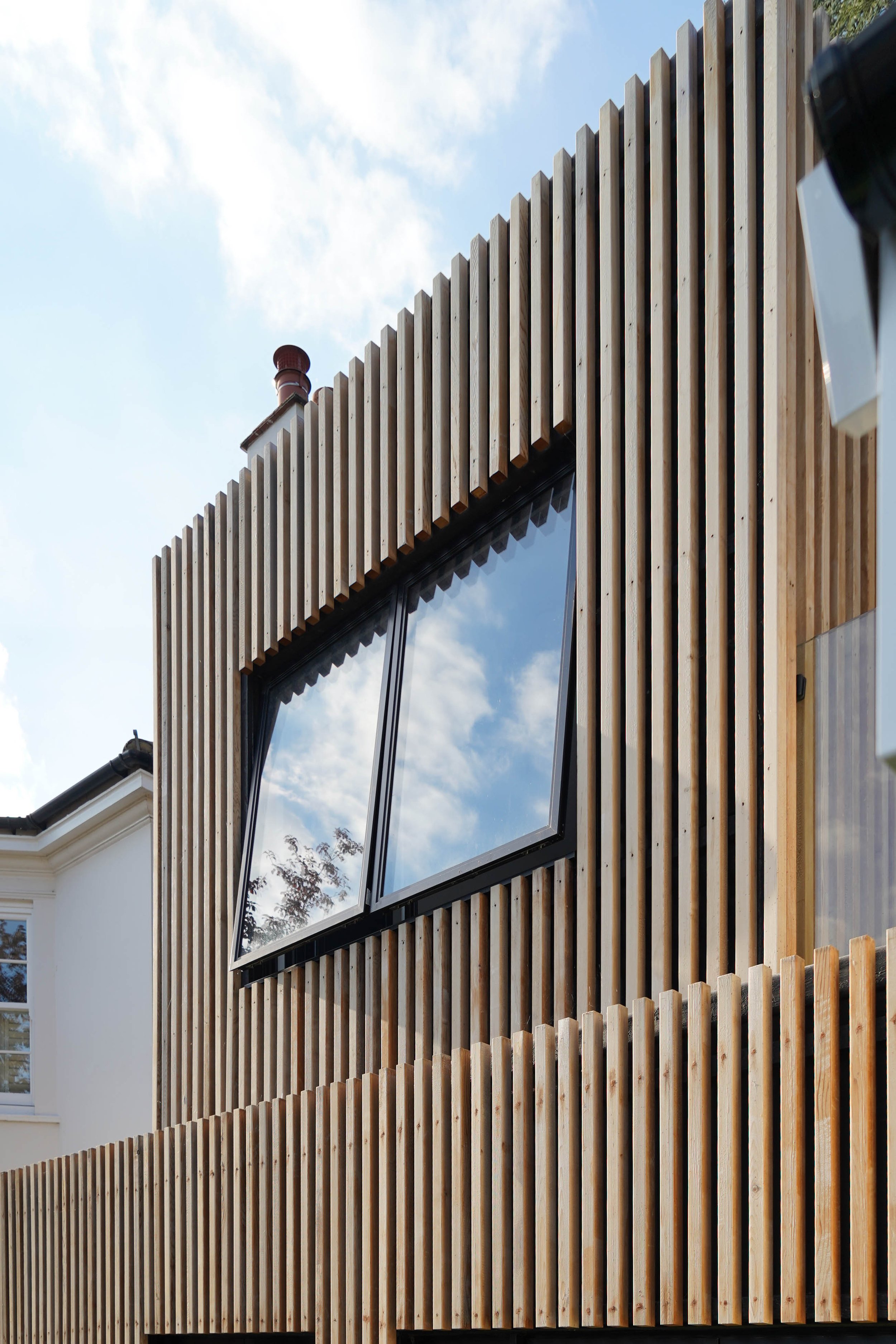 Modern building with vertical wooden slats and a large window reflecting the sky and clouds.
