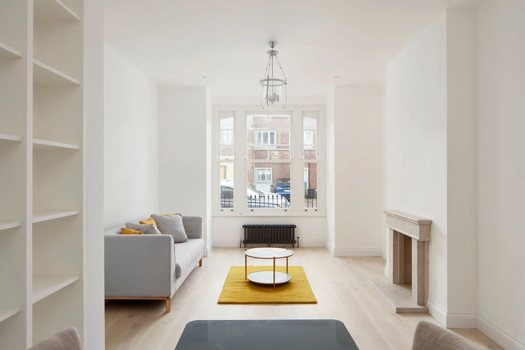 Bright living room with large window, sofa, yellow rug, circular coffee table, fireplace, and bookshelf, with minimal decor.