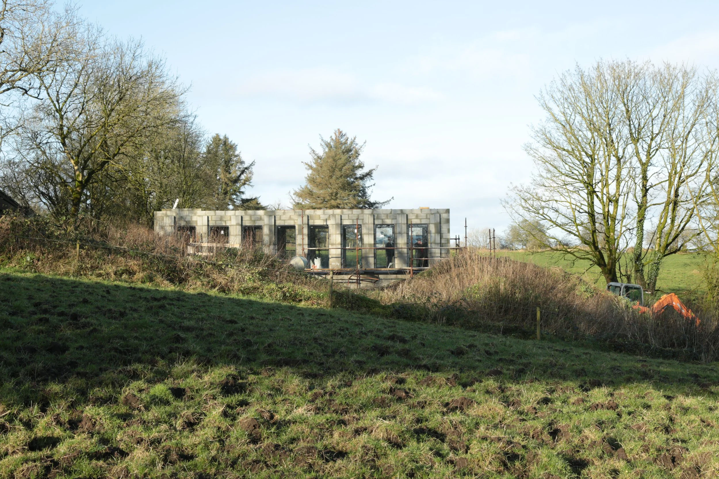 A building under construction with cement block walls, surrounded by trees and grassy terrain.