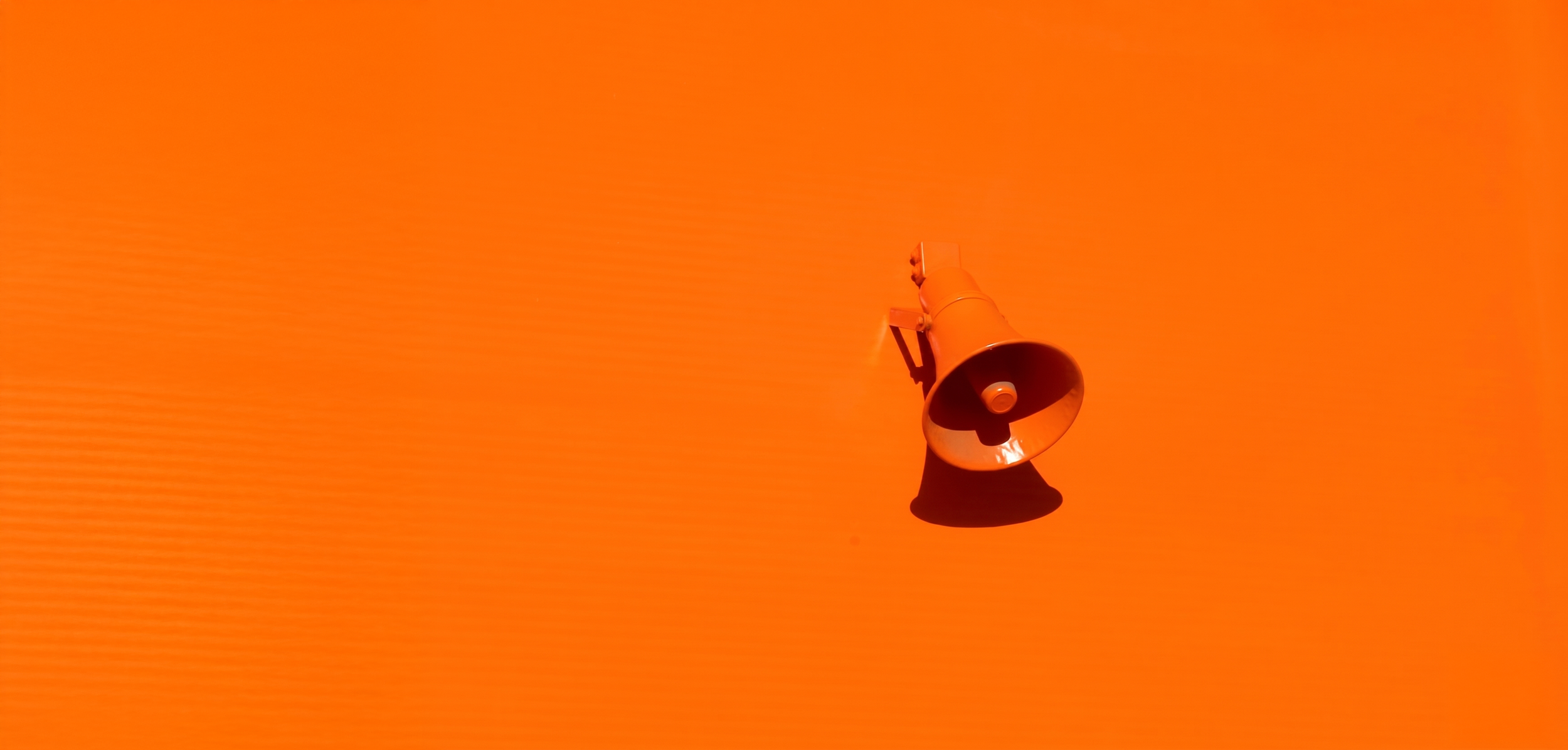 An orange wall with a white megaphone mounted on it, casting a shadow.