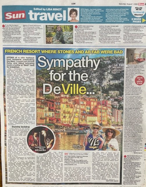 A newspaper page featuring a travel article about Aix-en-Provence, France. The main headline reads 'Sympathy for the DeVille,' with a large photo of a colorful hillside town with vibrant buildings along a waterfront. There is an image of two women wearing large hats in front of the water, and a smaller picture of two performers singing or speaking on stage. The page includes various columns and advertisements, mainly related to travel and tourism.