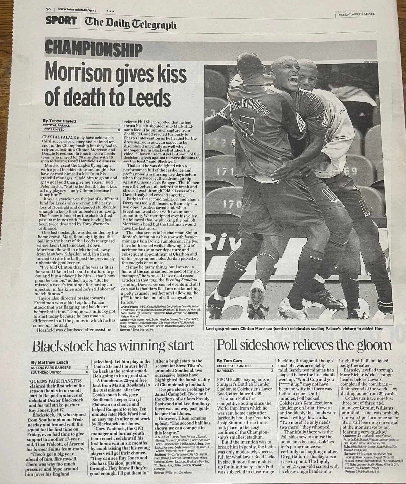 Black and white photo of Clinton Morrison celebrating a victory, hugging another person on a soccer field with a crowd in the background.