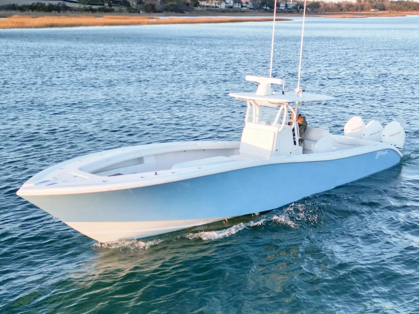 Center console boat moving on the water with four outboard engines, a T-top, and a crew member on board. 