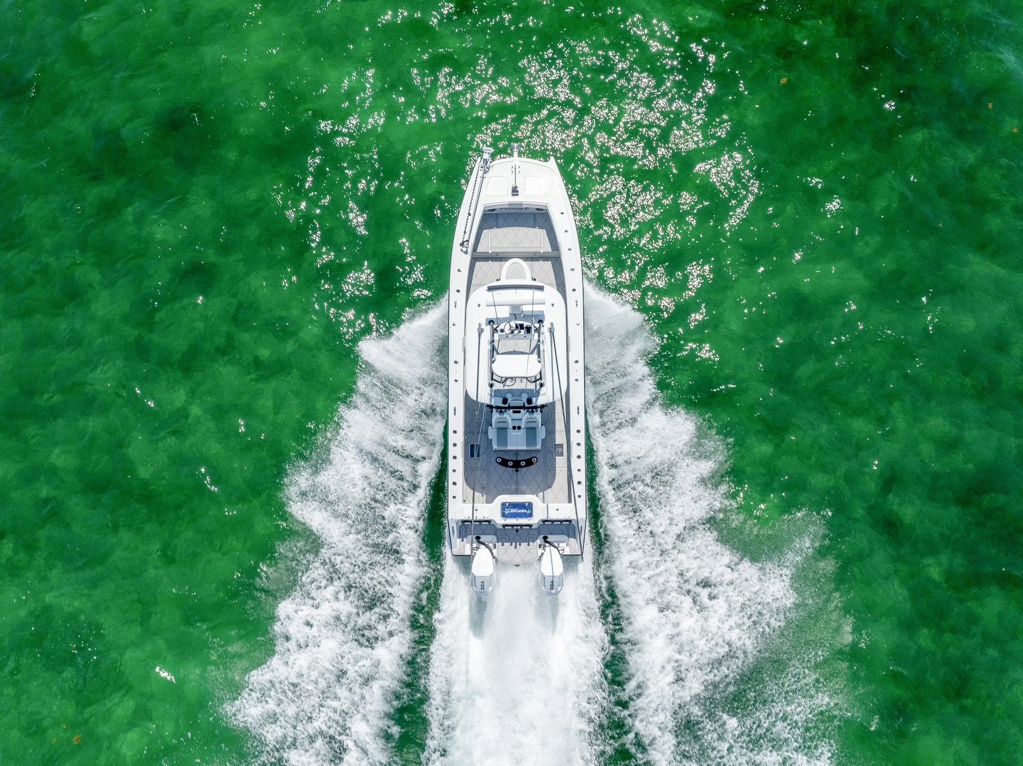 A white motorboat moving through green water, creating a wake behind it, viewed from above.