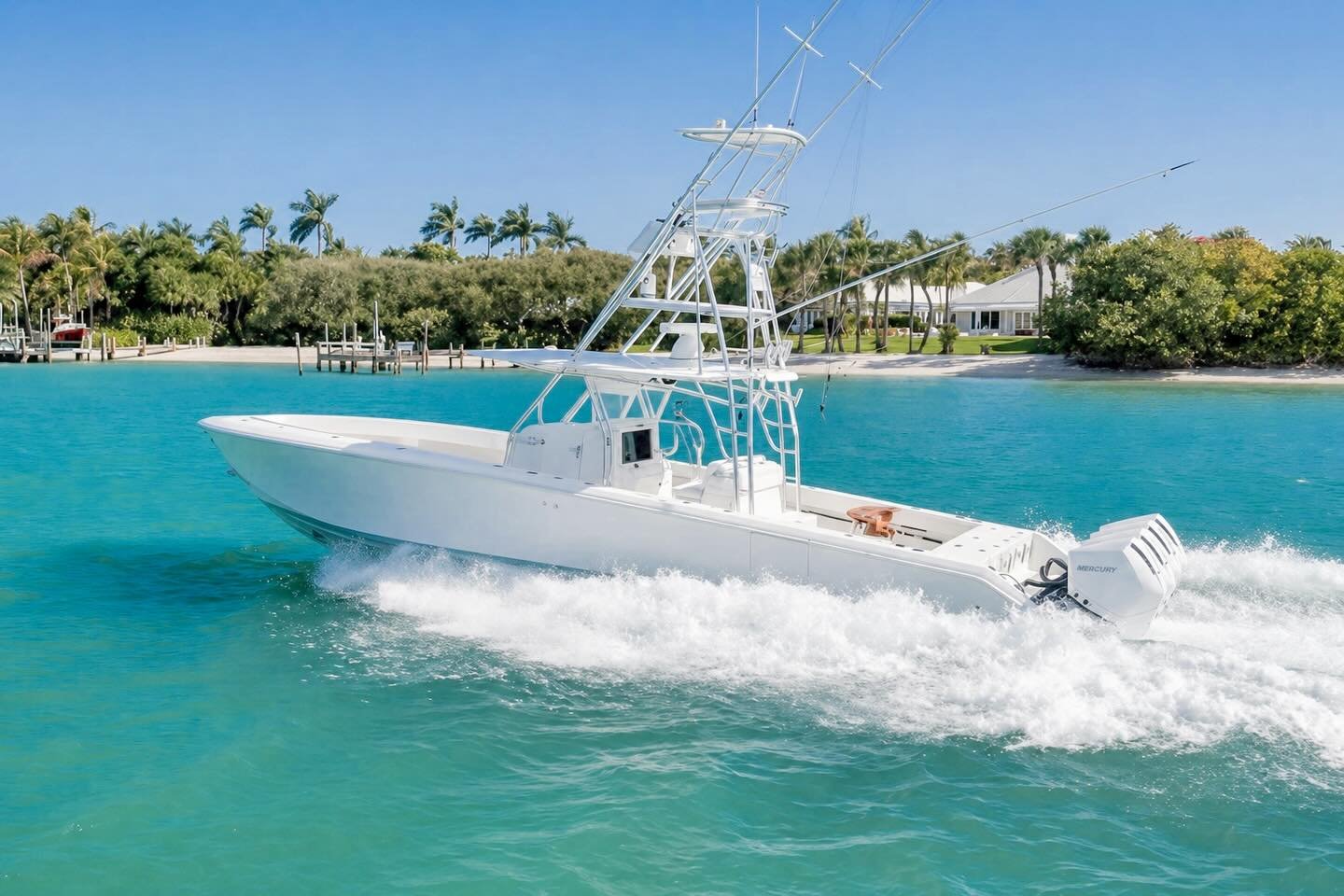 A white powerboat speeding through turquoise water with houses and palm trees on the shoreline in the background.