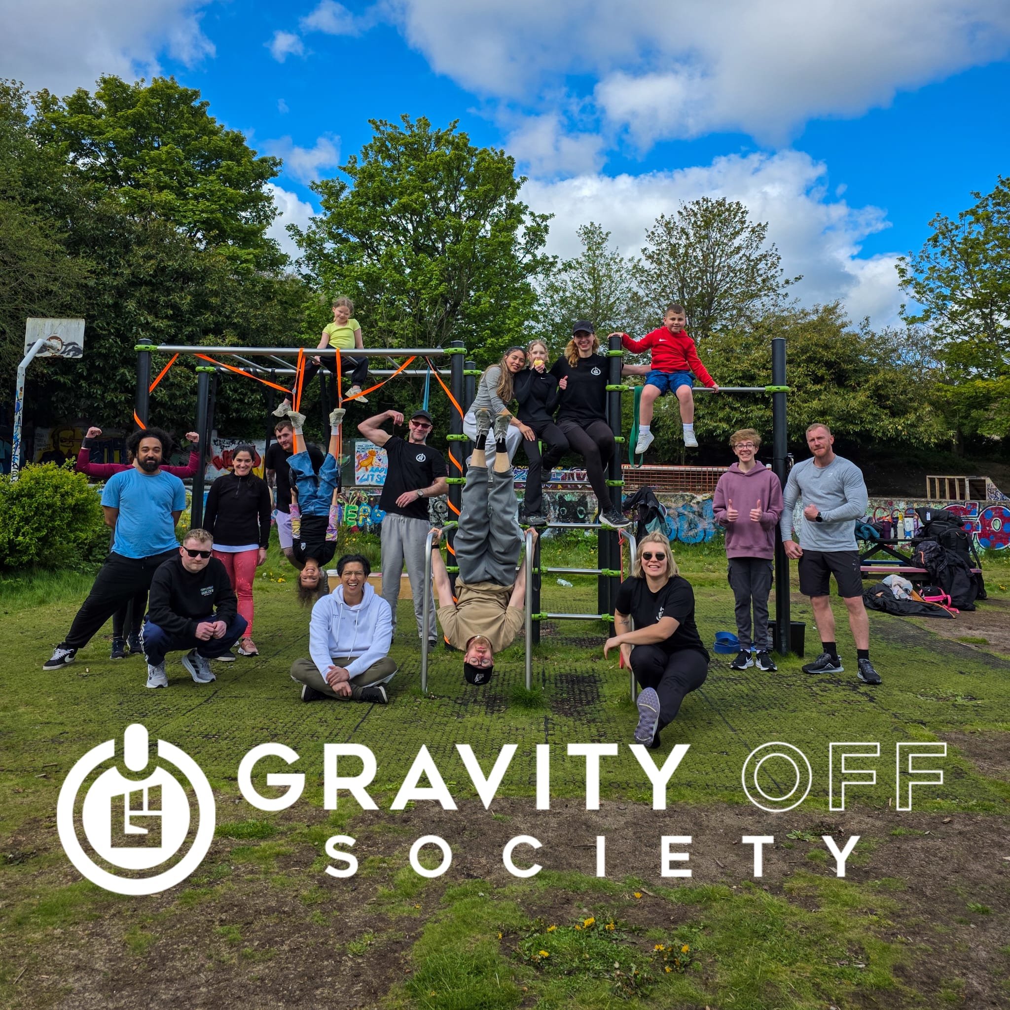 A group of people outdoors at a park or playground, sitting or standing on a climbing structure, with trees and blue sky with clouds in the background, and a large overlay text reading 'Gravity Off Society'.