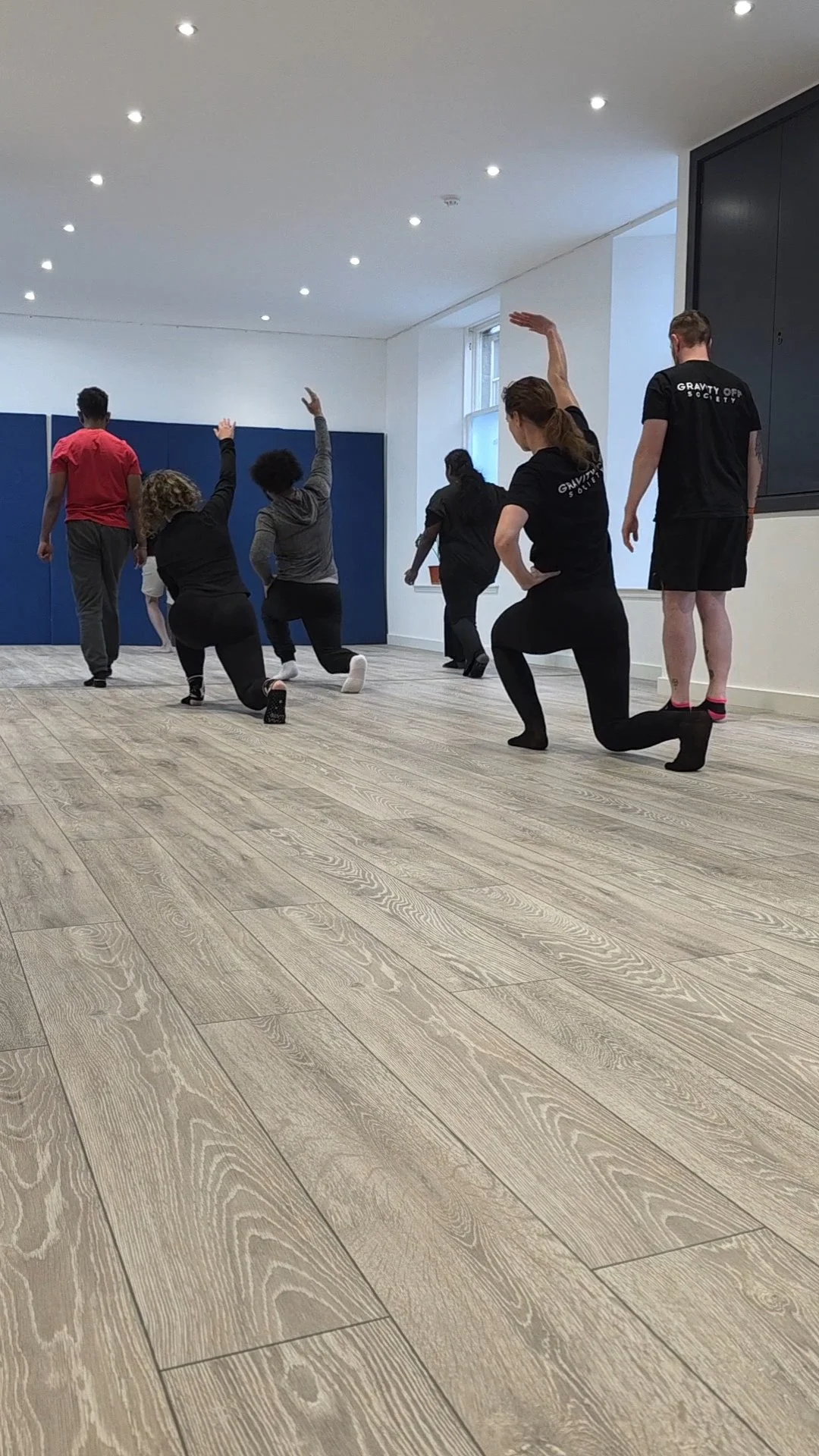 A group of people participating in a yoga or meditation class in a bright, modern studio with wooden flooring and white walls.