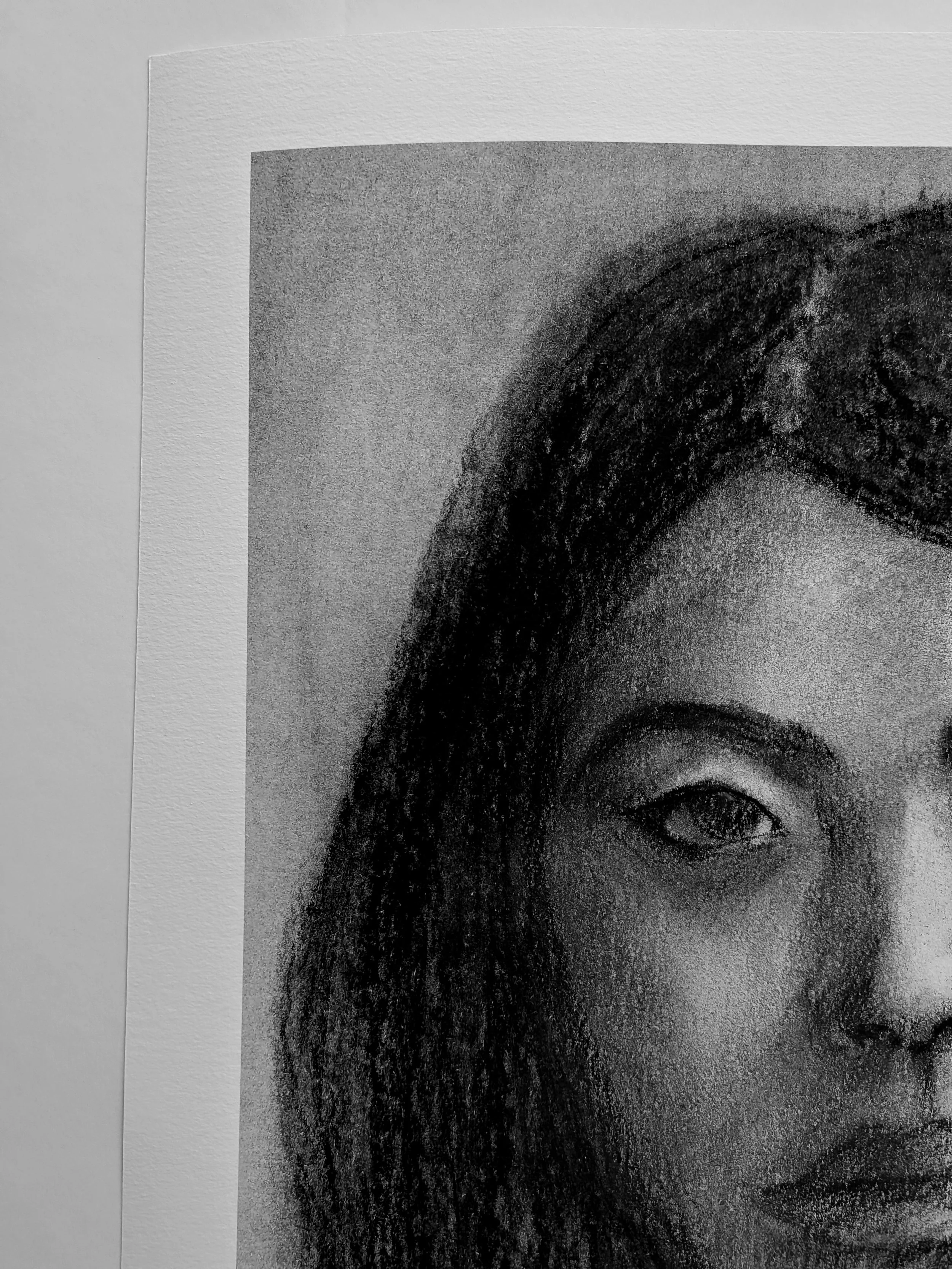 A close-up black and white print of a woman's face, showing her eye, eyebrow, and part of her forehead and lips, on a piece of paper pinned to a white wall.