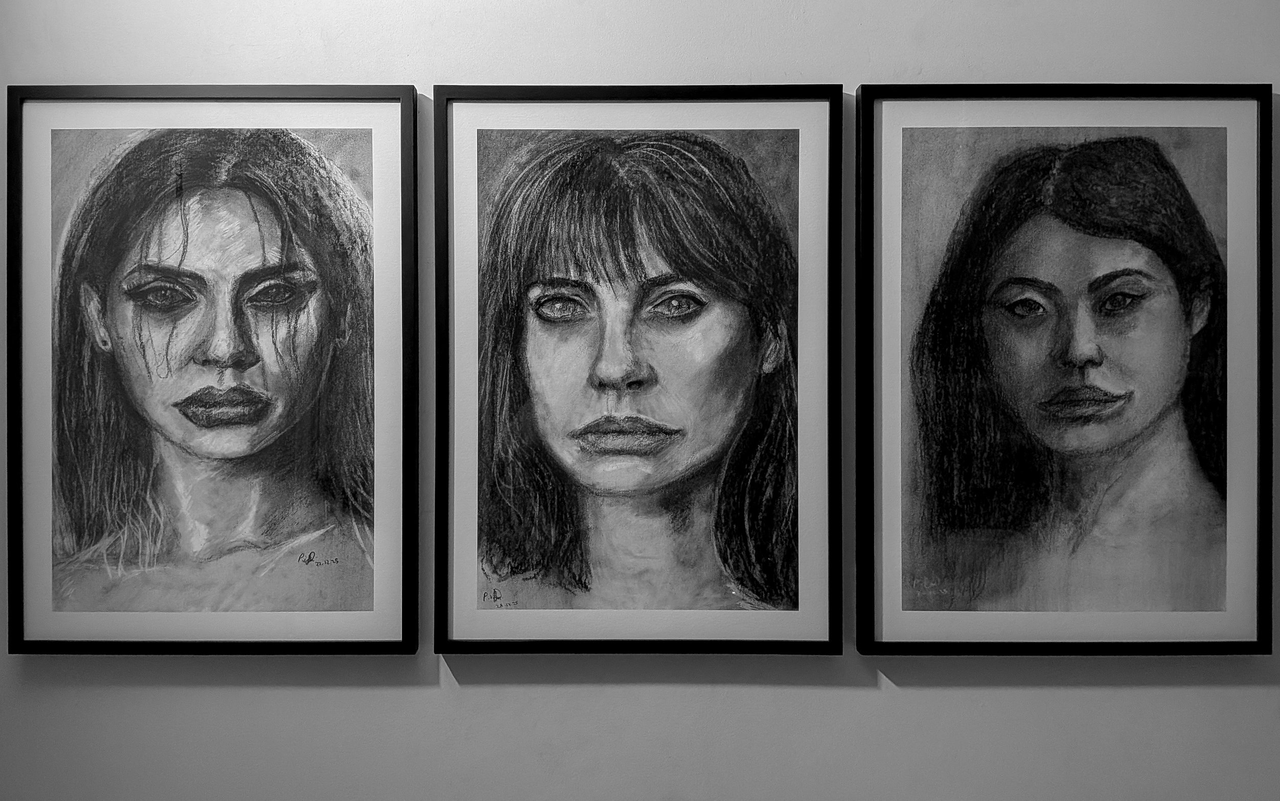 Three black and white framed portrait drawings of women's faces hung on a wall.
