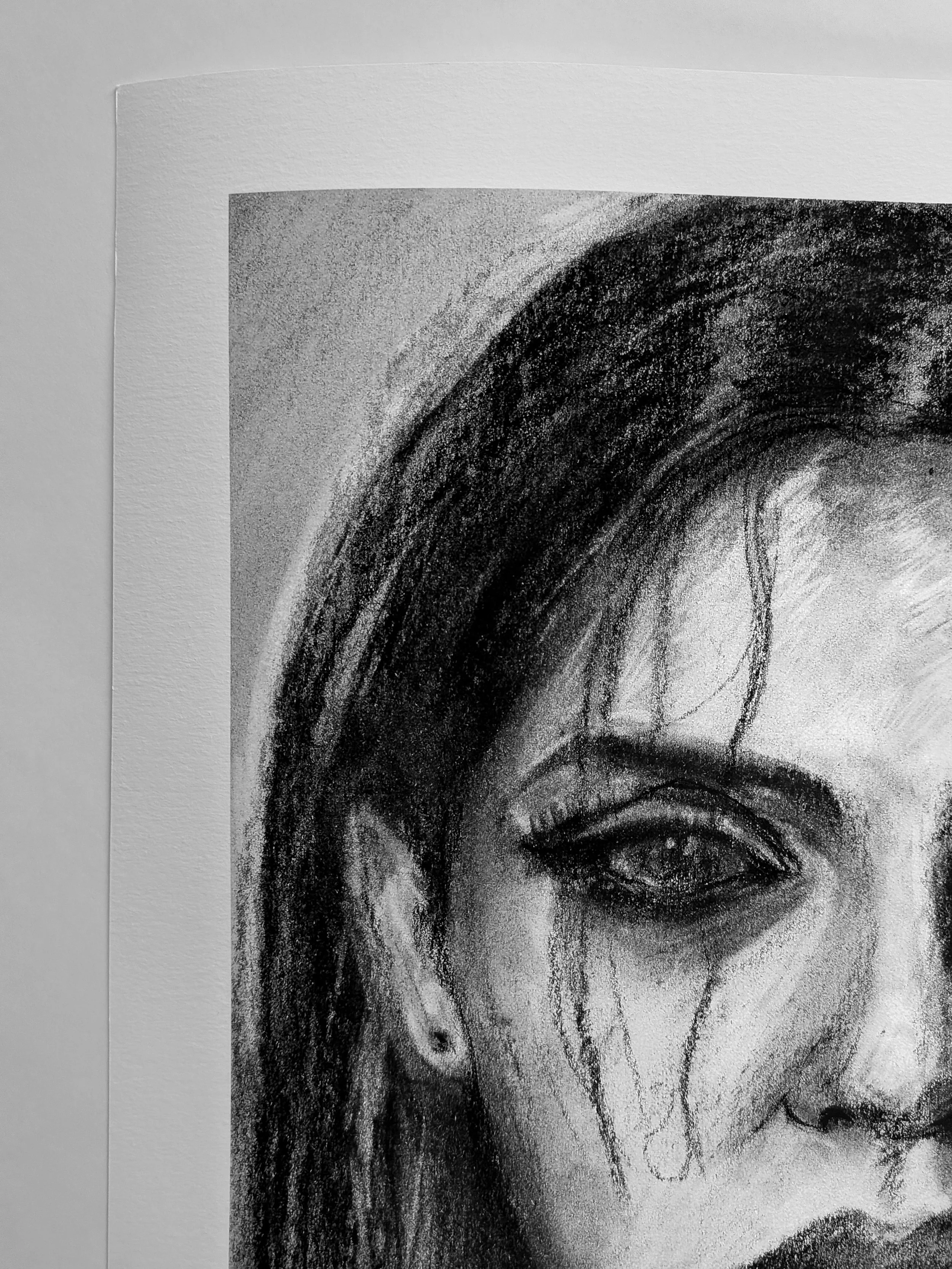 Close-up of a charcoal drawing of a woman's face with long hair, an earring, and dark makeup around the eye, on textured white paper.