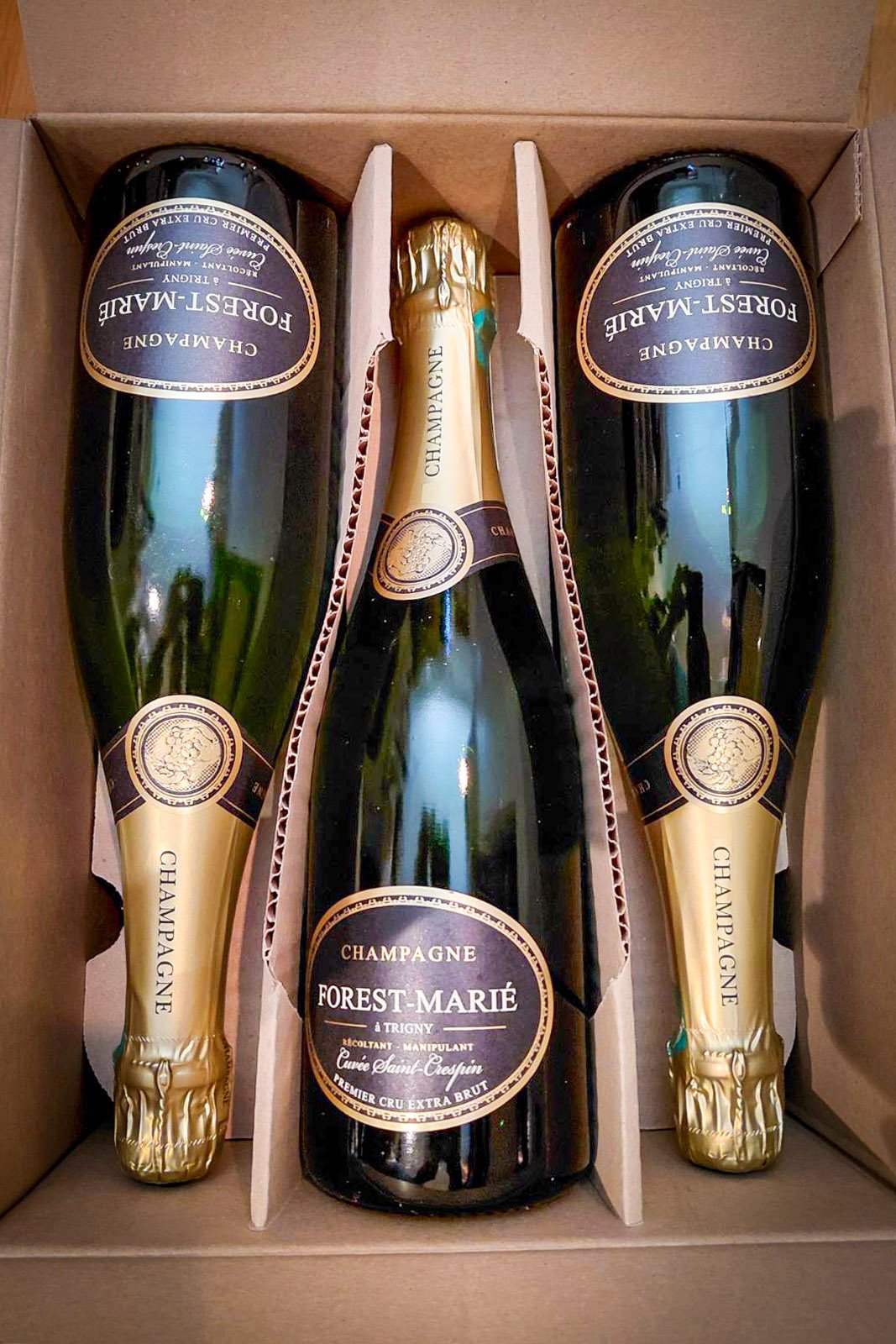 A box containing one bottle of Forest-Marie champagne and two foil-wrapped champagne bottles.