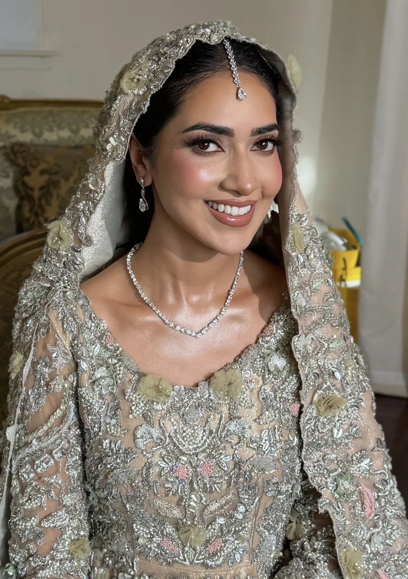 Close-up of a woman smiling, dressed in traditional South Asian bridal attire with intricate embroidery, jewelry, and a veil.