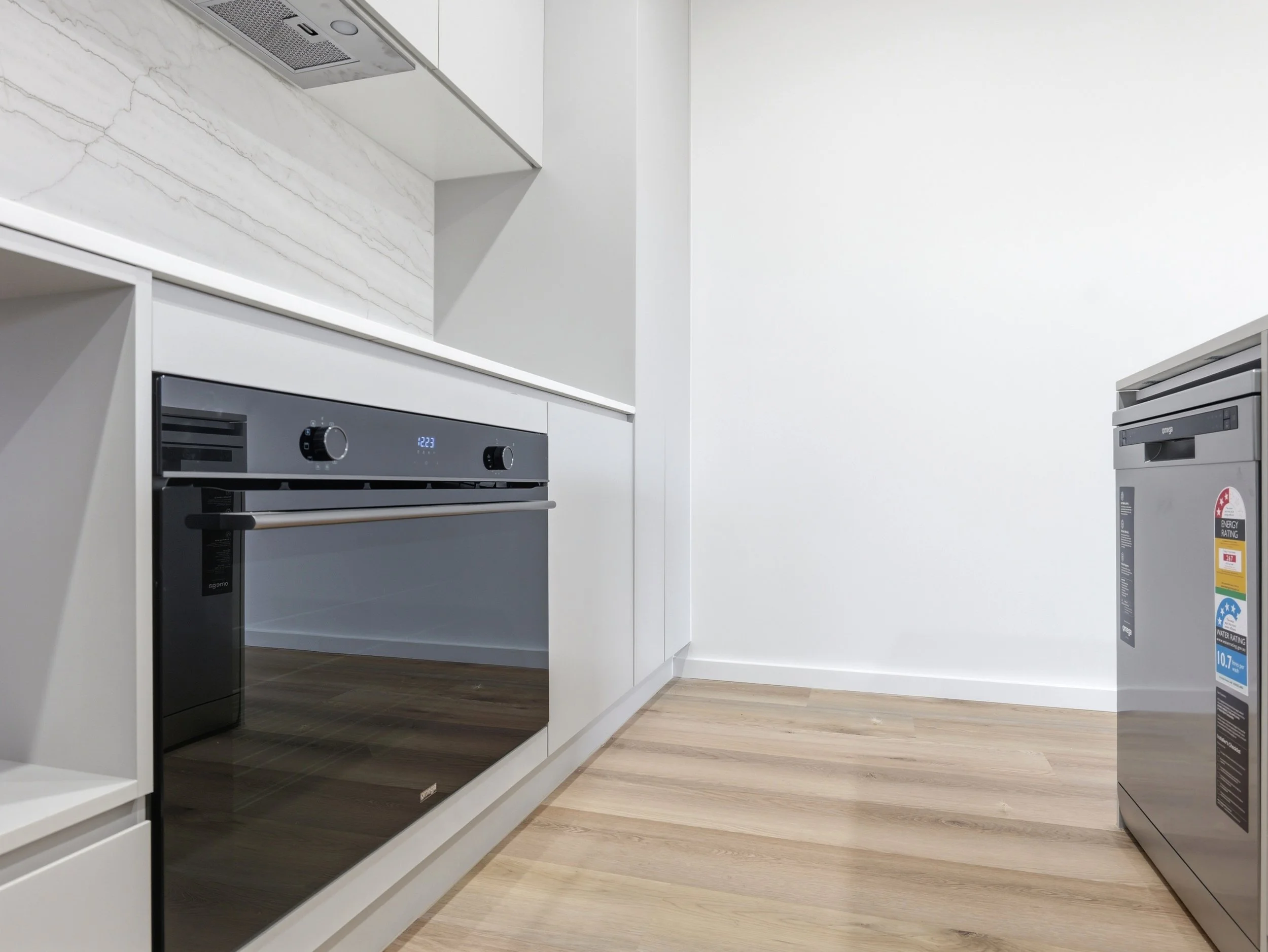 Modern kitchen with white cabinetry, built-in oven, and a laundry dryer with water ratings indicators.