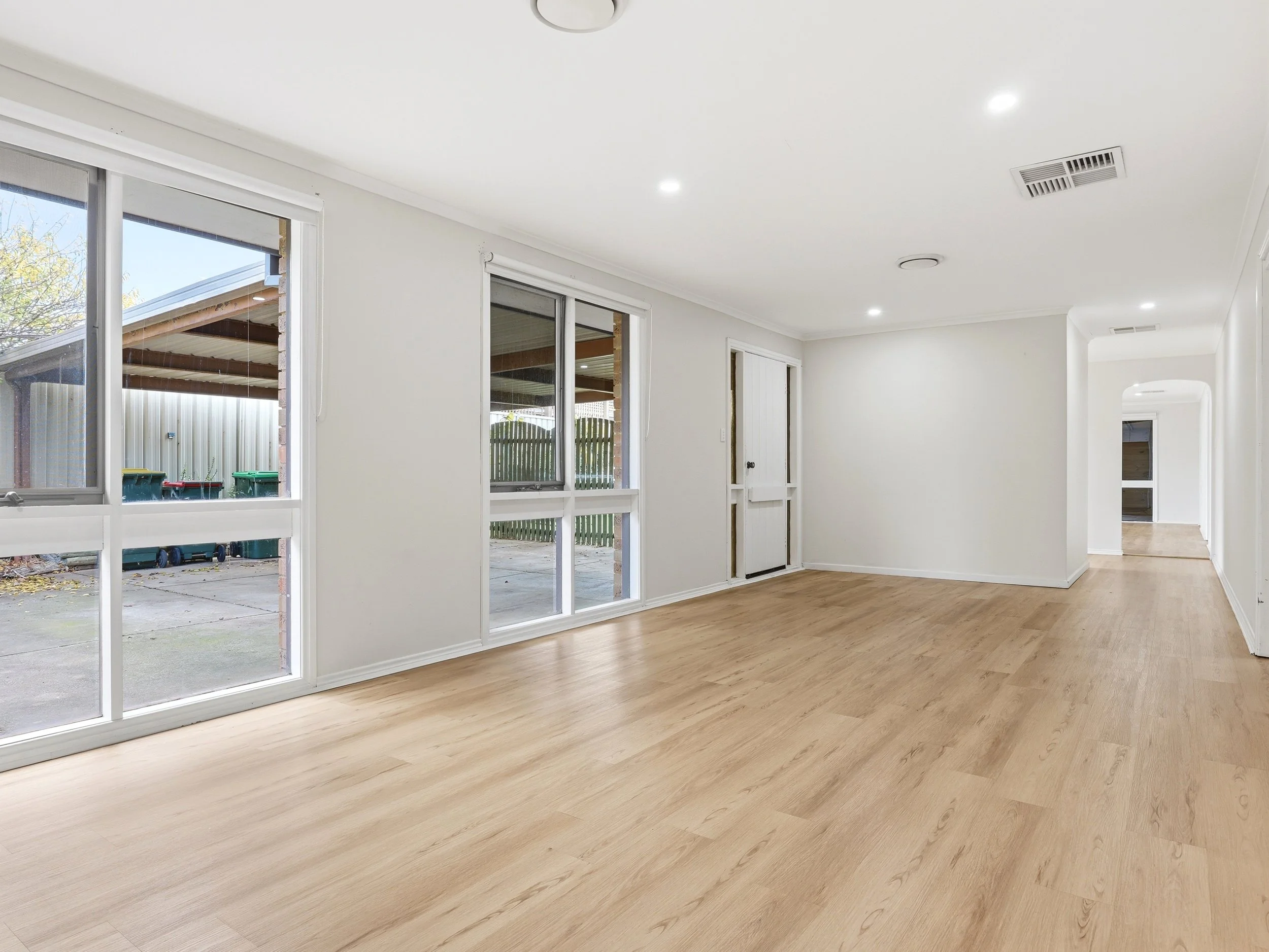 Empty living room with large sliding glass doors, white walls, hardwood floors, and recessed ceiling lights.
