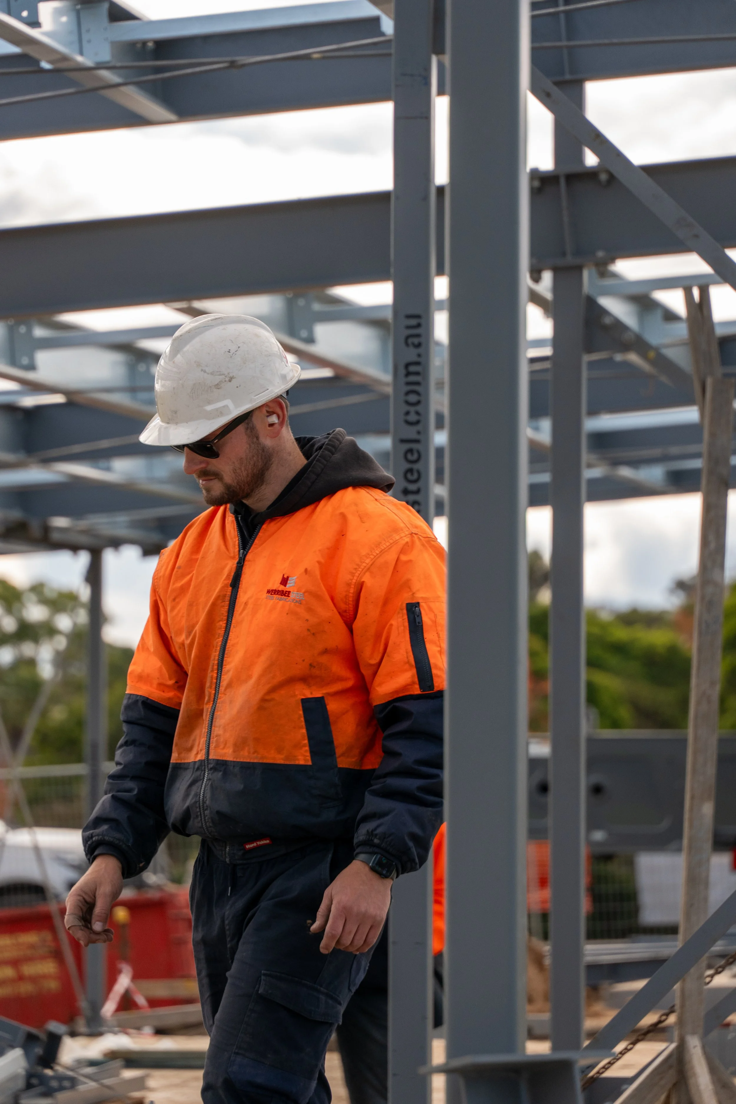 Man wearing safety helmet and sunglasses working outdoors at a construction site with steel framing.