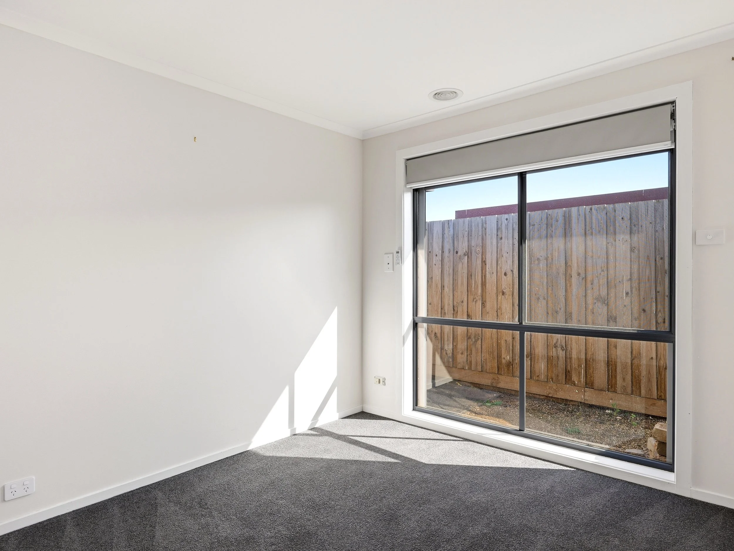 Empty room with white walls, gray carpet, and sliding glass door leading to a fenced outdoor area.