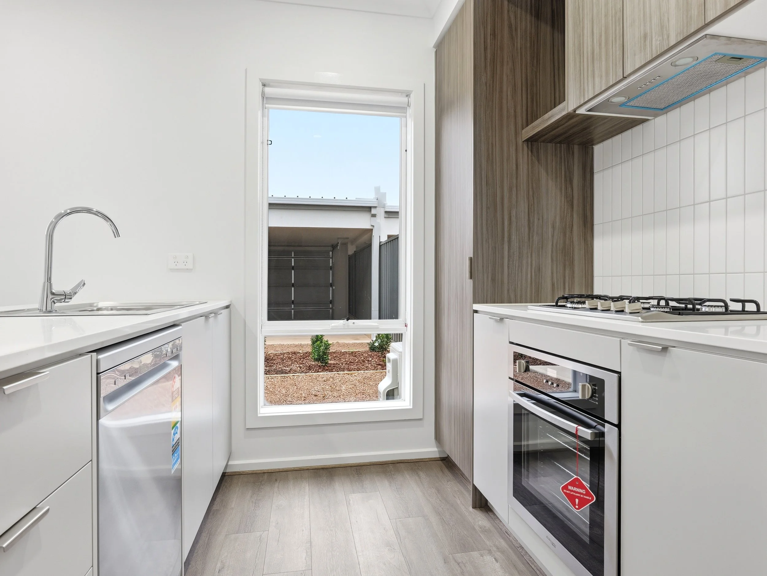 Modern kitchen with white cabinets, wooden wall panels, a stove, and a door leading outside to a small yard with plants.
