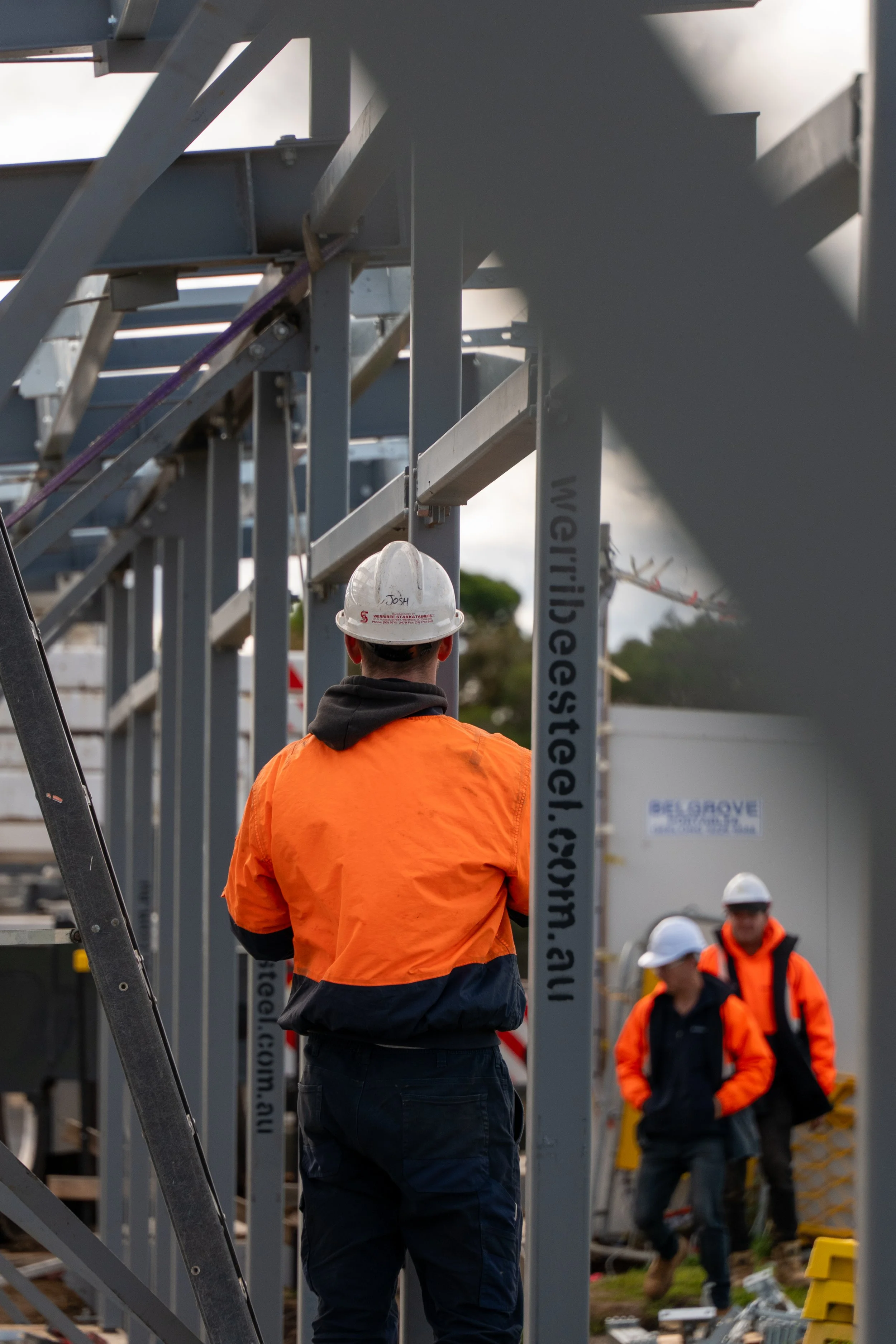Construction workers wearing safety gear and orange jackets working on steel framework at a construction site.