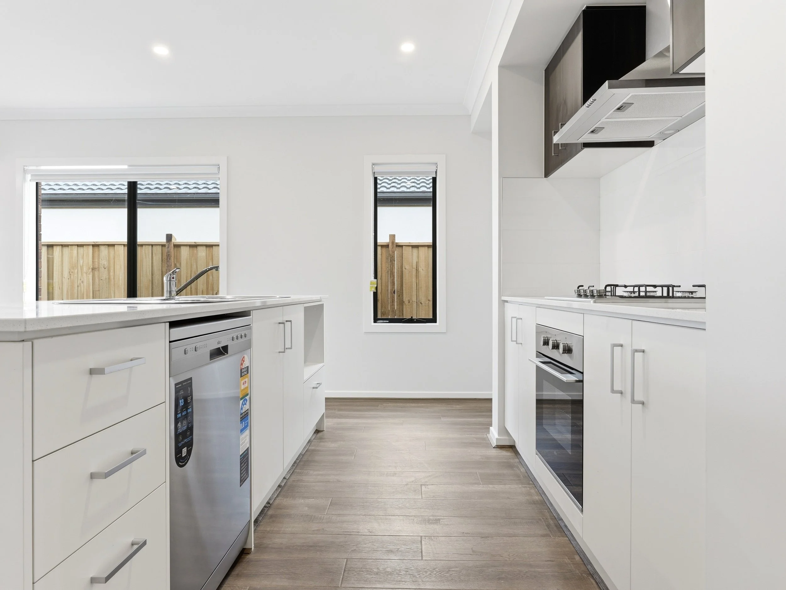 Modern kitchen with white cabinets, stainless steel appliances, a double sink, and two vertical windows overlooking a backyard with a wooden fence.