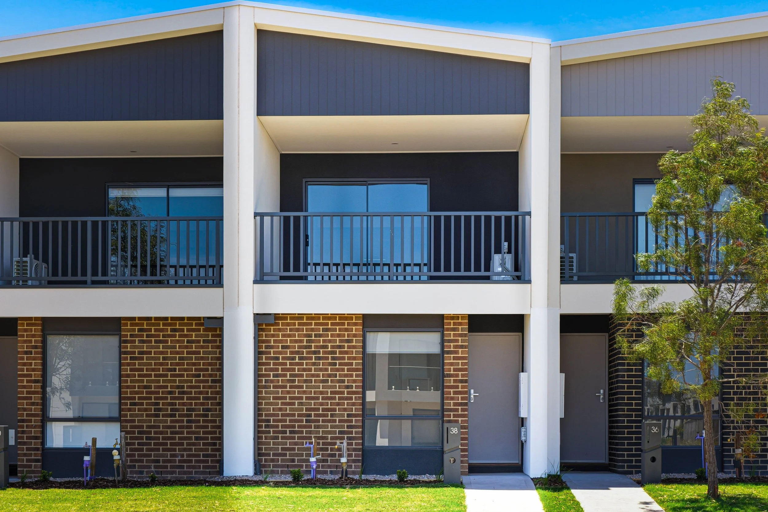 Front view of modern multi-story apartment building with brick and siding exterior, small front yard with grass, and trees