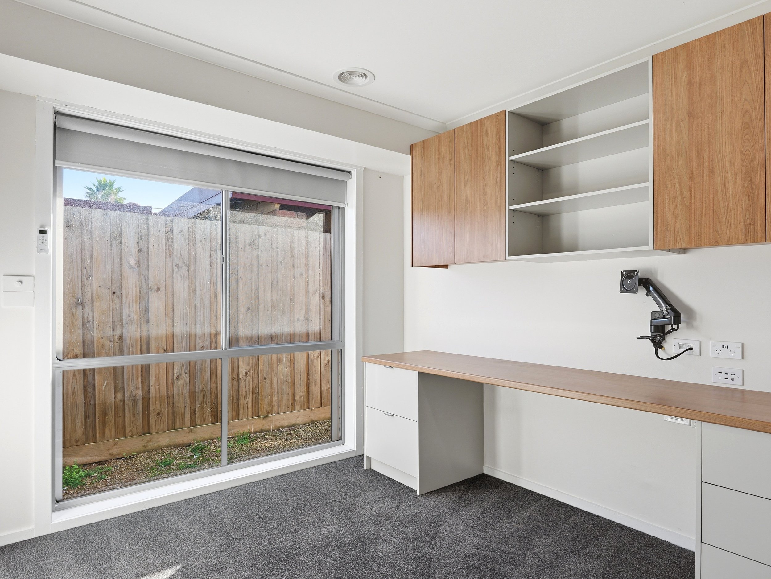 Interior of a room with a large sliding glass door leading to an outdoor wooden fence, white walls, and a black adjustable desk lamp mounted on the wall.
