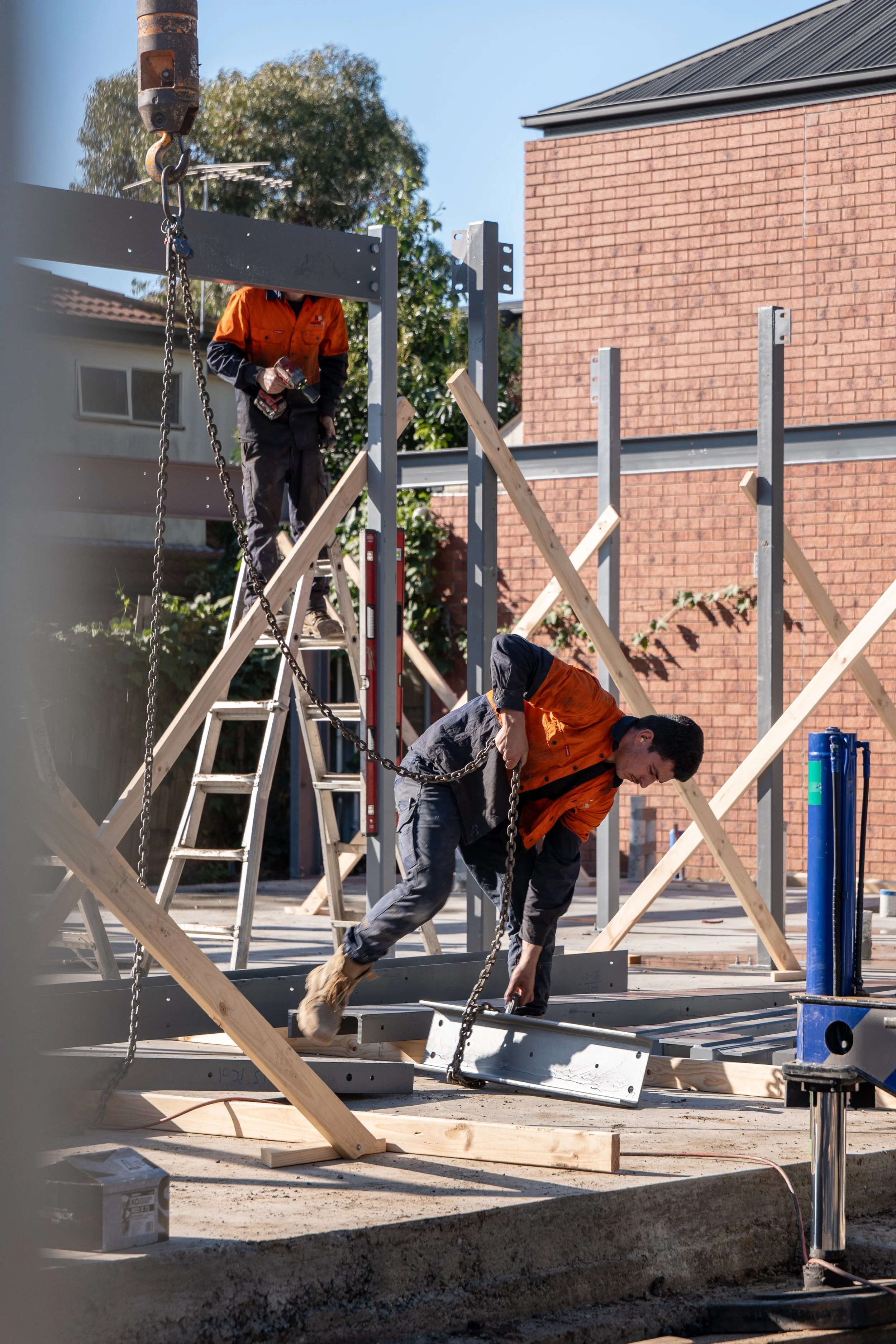 Construction workers assembling metal frames with wooden support beams at an outdoor construction site.