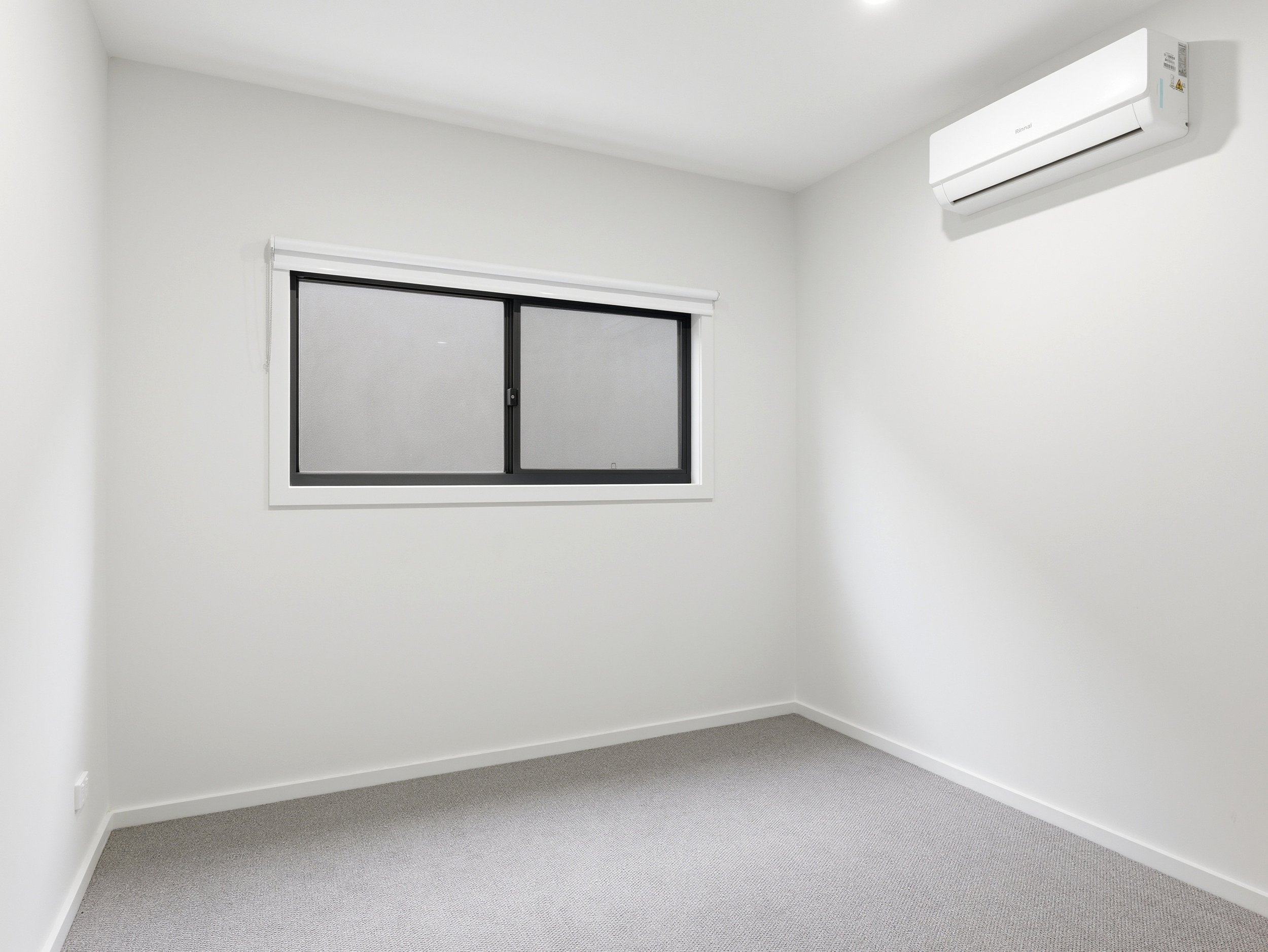 Empty white room with a single window and an air conditioning unit mounted on the wall.