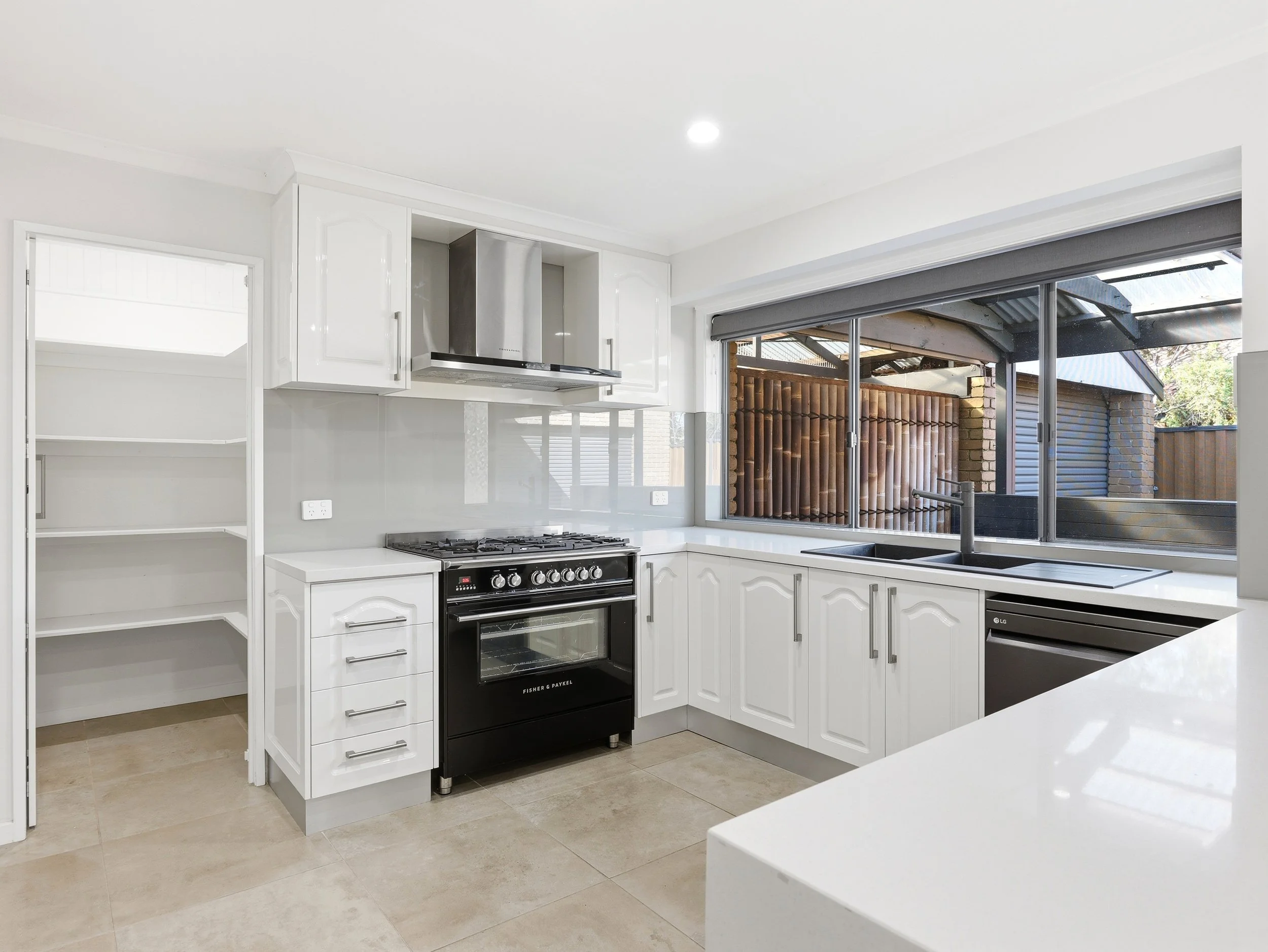 Modern kitchen with white cabinets, black stove, large window, and outside view of a deck and trees.