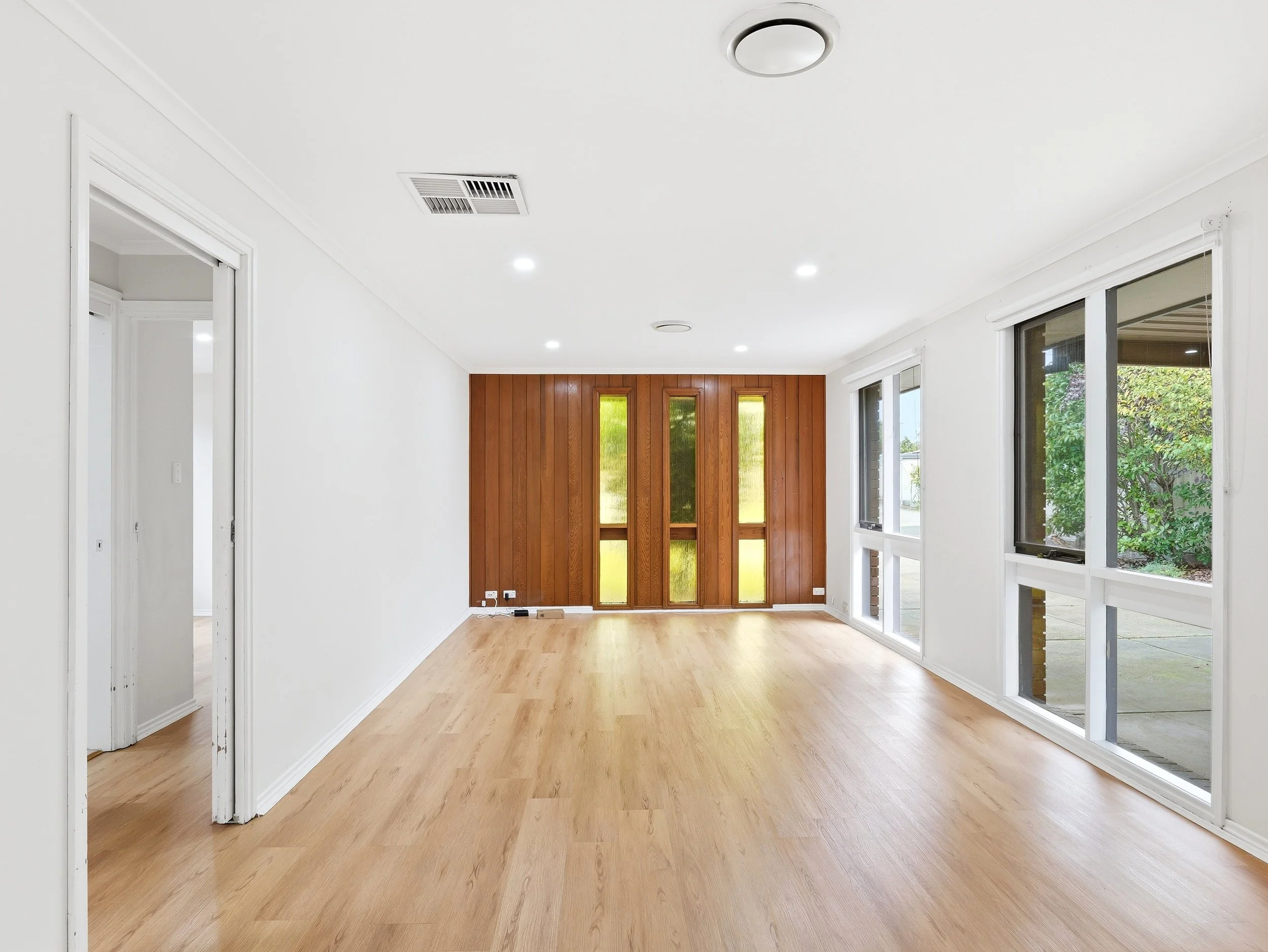Empty room with white walls, hardwood floors, large windows, and a wooden door at the end.