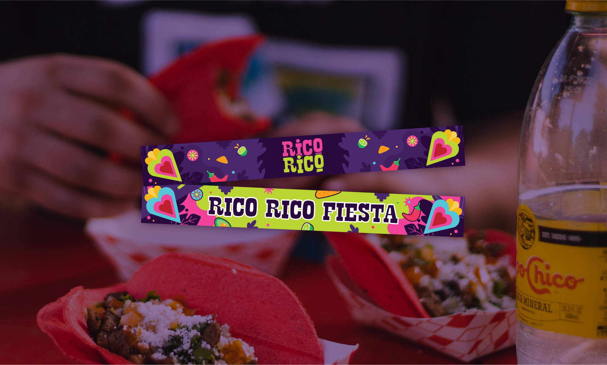 Colorful Fiesta snacks with two colorful ribbons reading 'Rico Rico' and 'Rico Rico Fiesta' in the foreground, a hand holding a red taco in the background, a clear water bottle on the right, and various Mexican dishes on a red table.