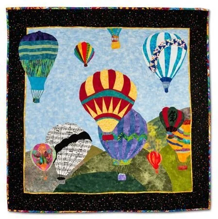 Colorful quilt with hot air balloons flying over green hills, set against a sky with clouds.